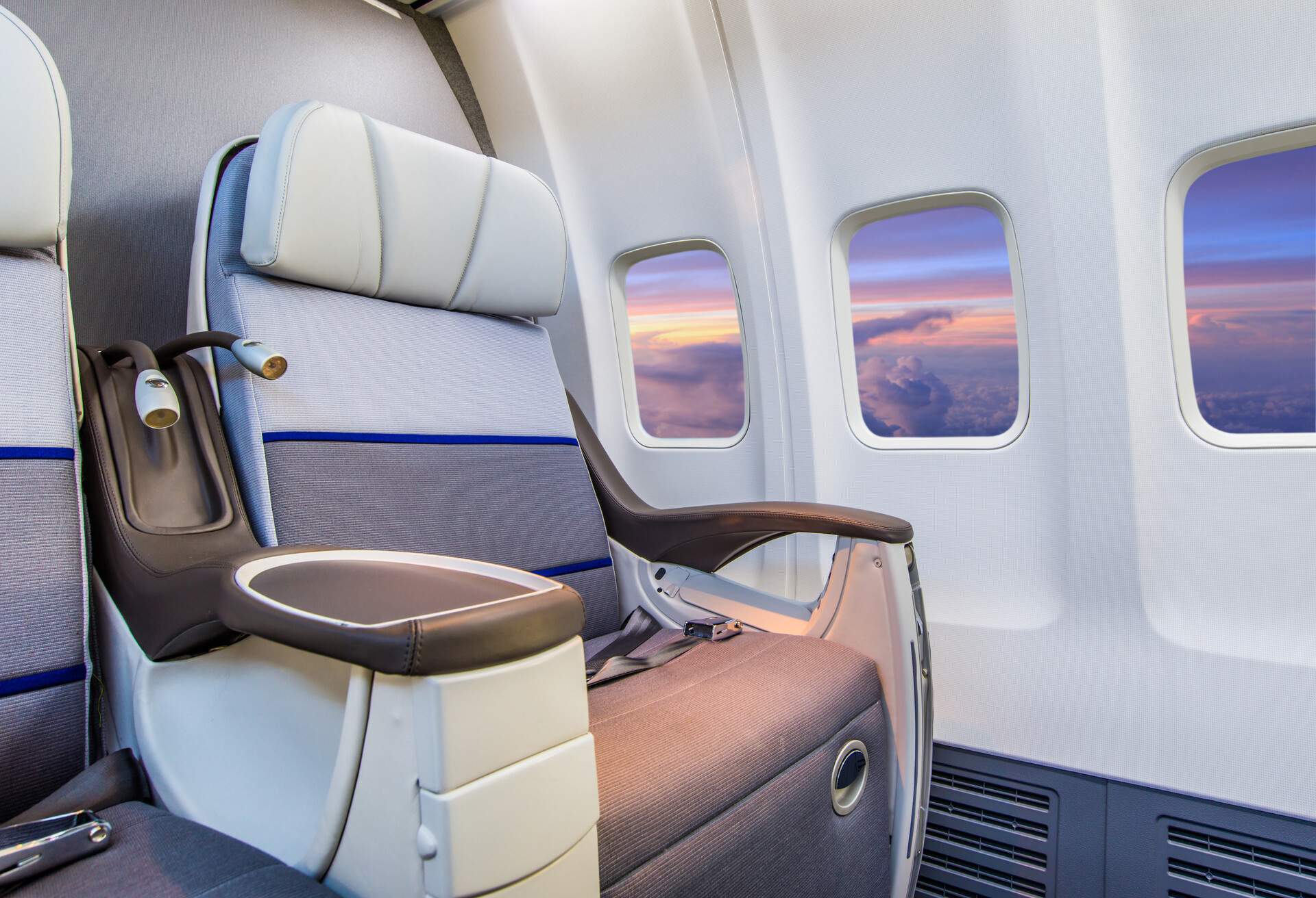 An empty business-class window seat inside an airplane with a scenic sky view.