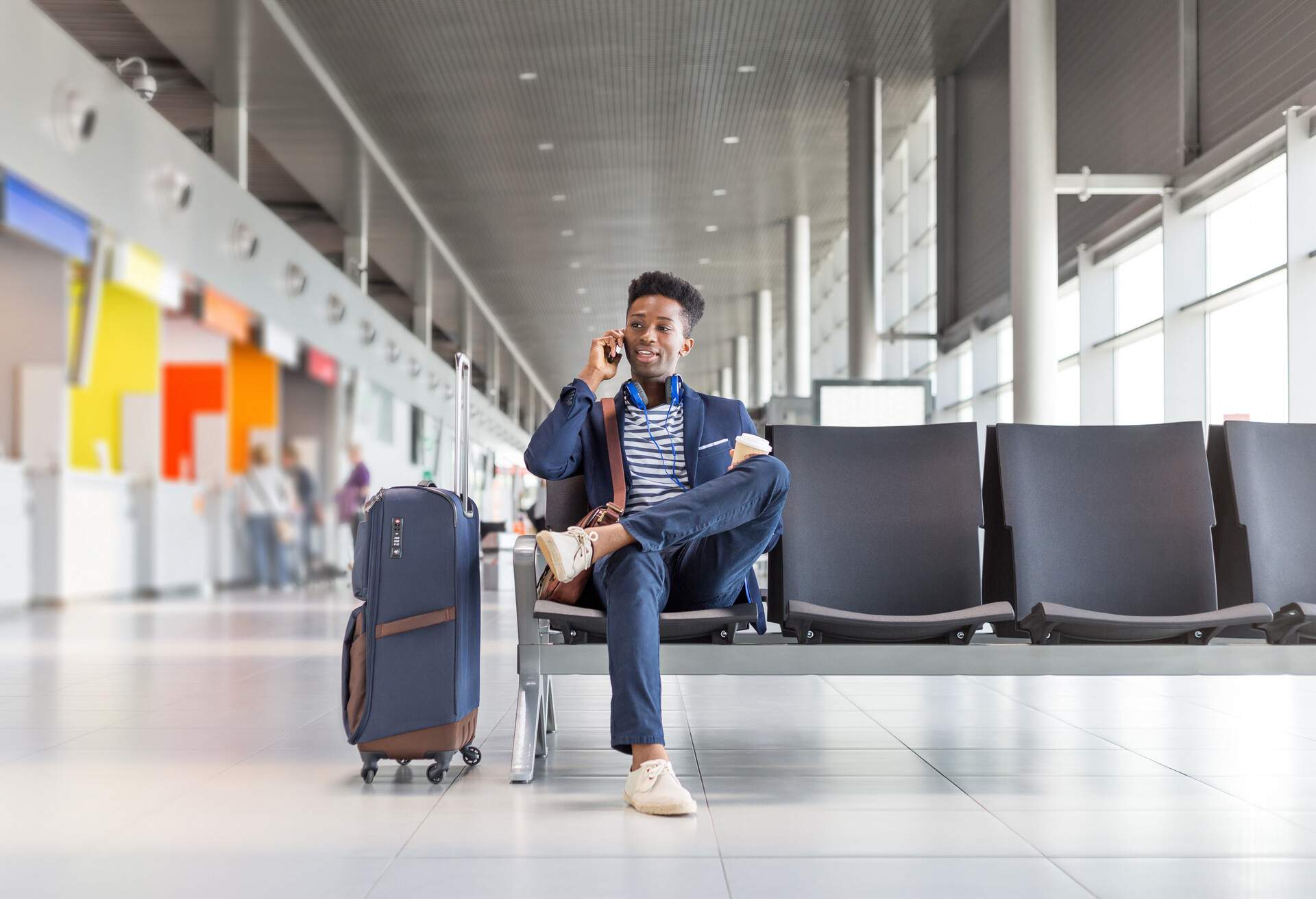 A male traveller talking to someone on his smartphone while waiting for his flight at the airport lounge.