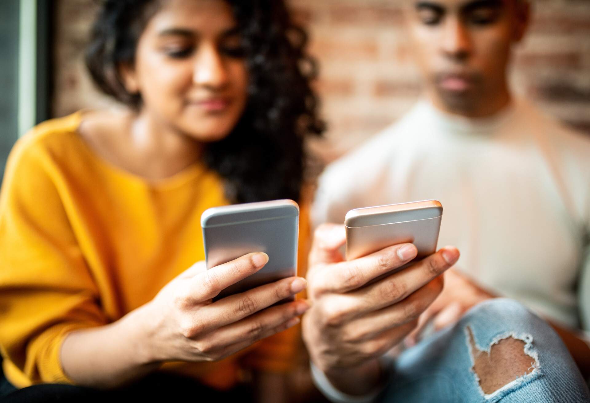 Two friends in vibrant clothes stare at their phones.