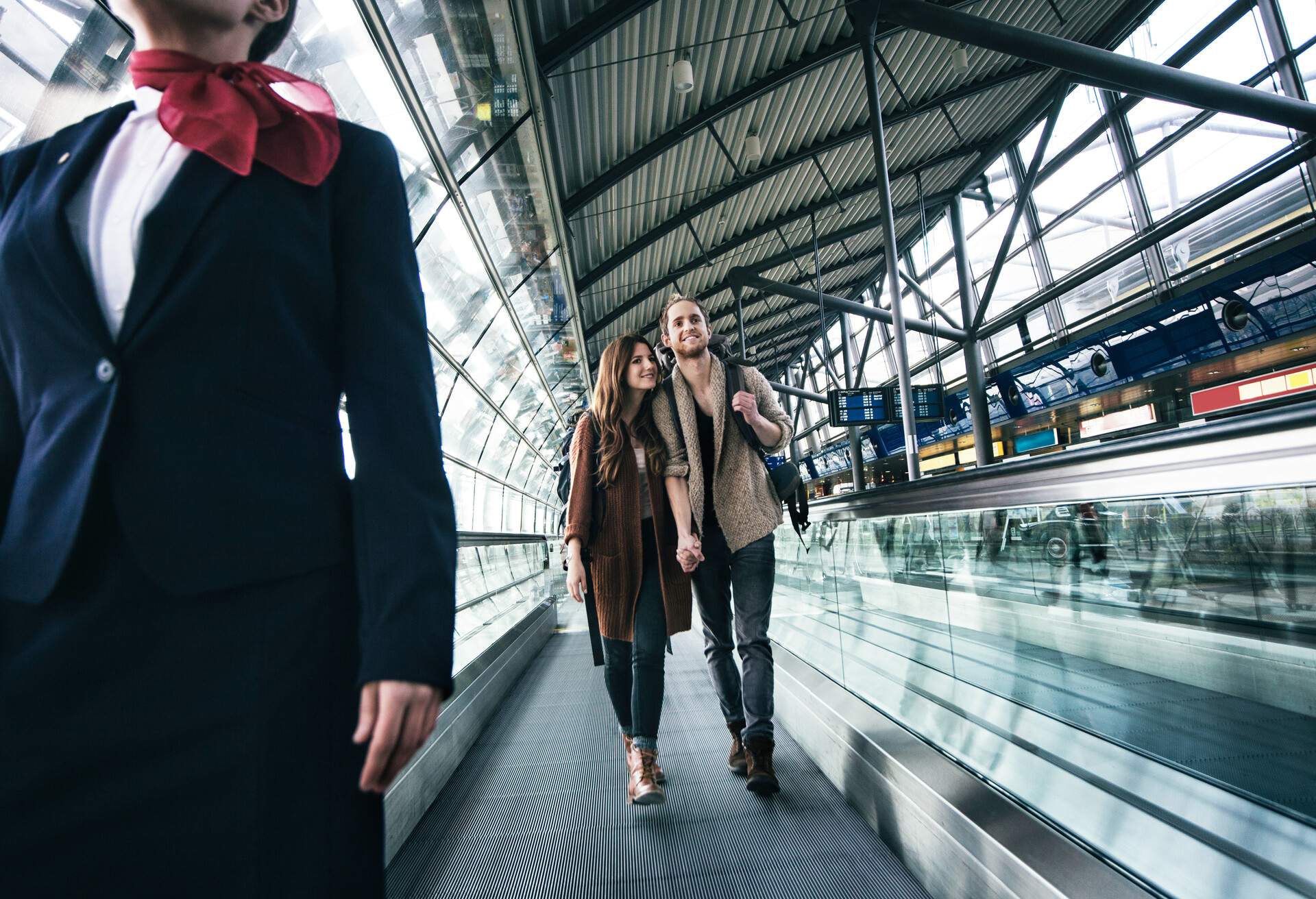 A young couple walking on an inclined moving walkway at an airport.