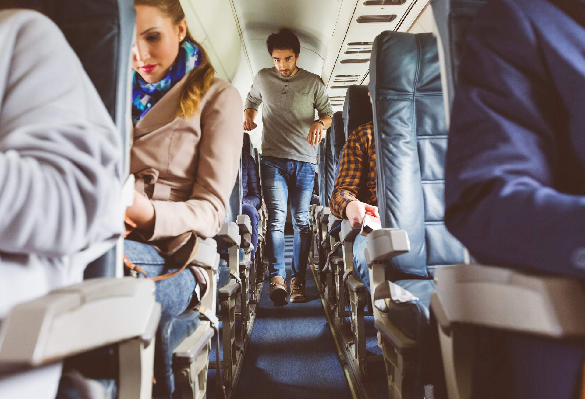 A man walks on an airplane cabin's aisle across seats with sitting passengers.