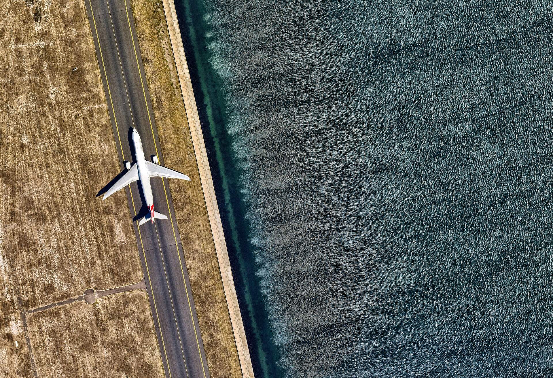 A white airplane on the runway alongside the ocean.