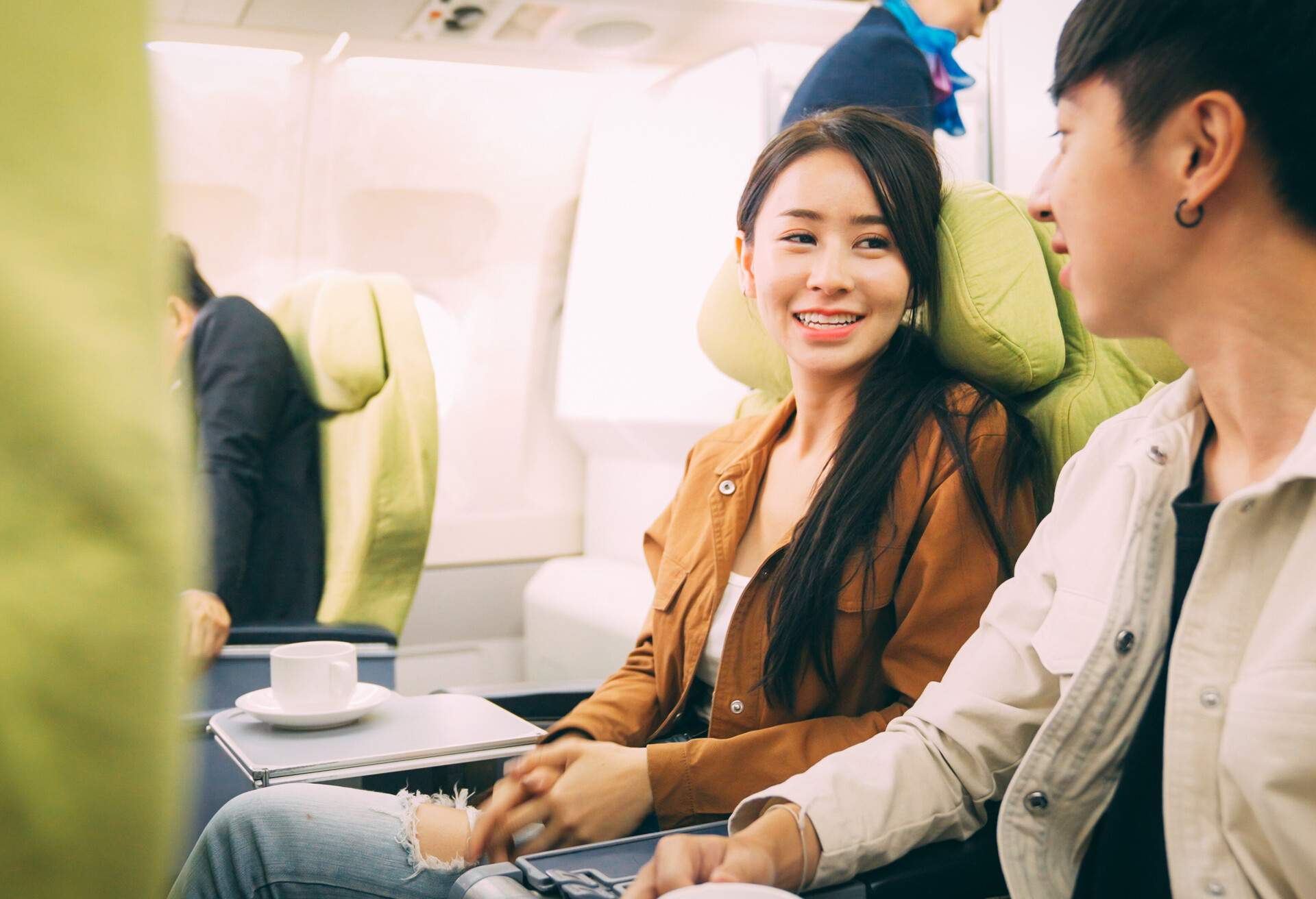 A young Asian couple engaged in a lively conversation on an airplane, their faces radiating happiness.