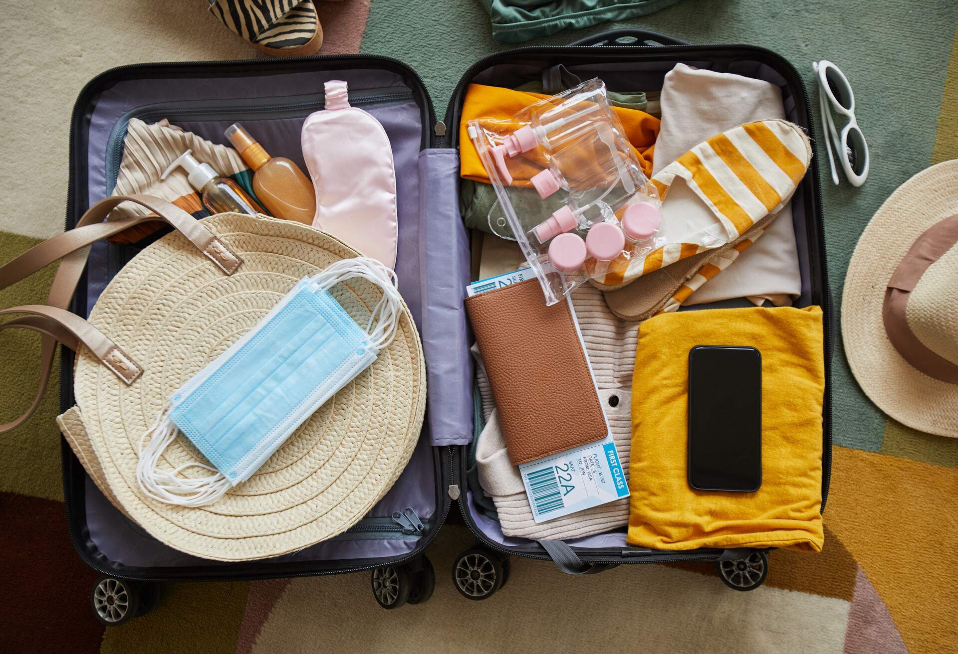 Luggage with colourful travelling essentials with facemasks, refillable bottles and a passport.