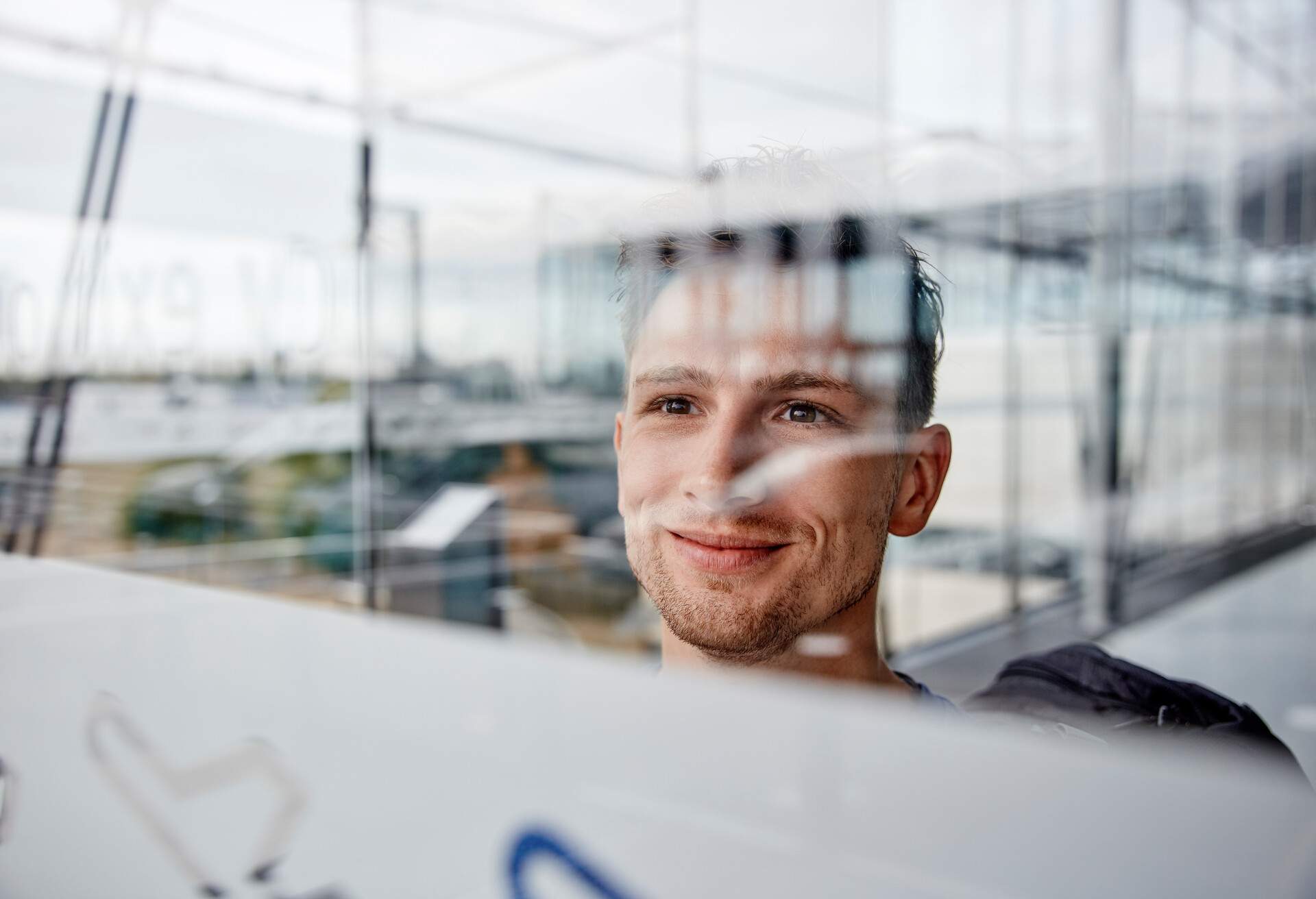 A person stands by a glass window, smiling as they gaze outward.