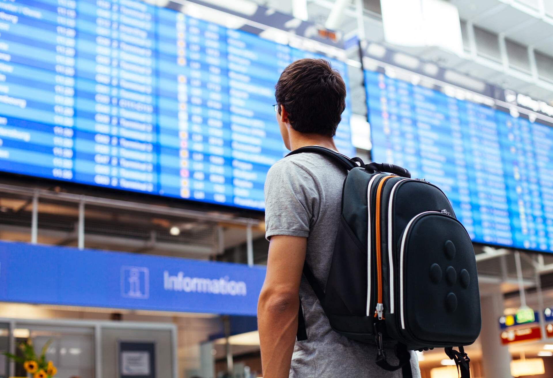 A man carrying a backpack checking the flight information display at the airport.