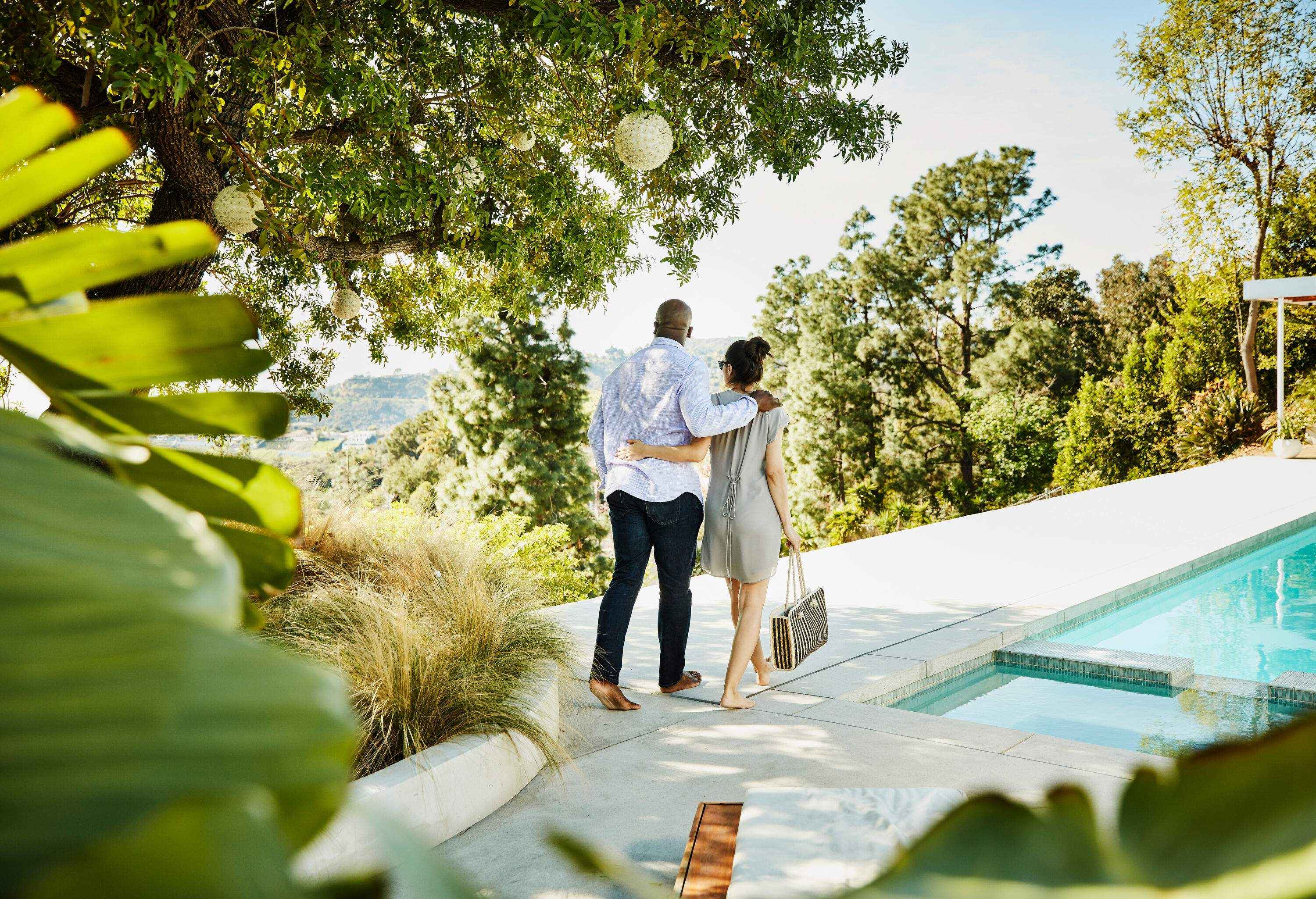 A couple embraces while walking beside a pool amongst lush foliage.