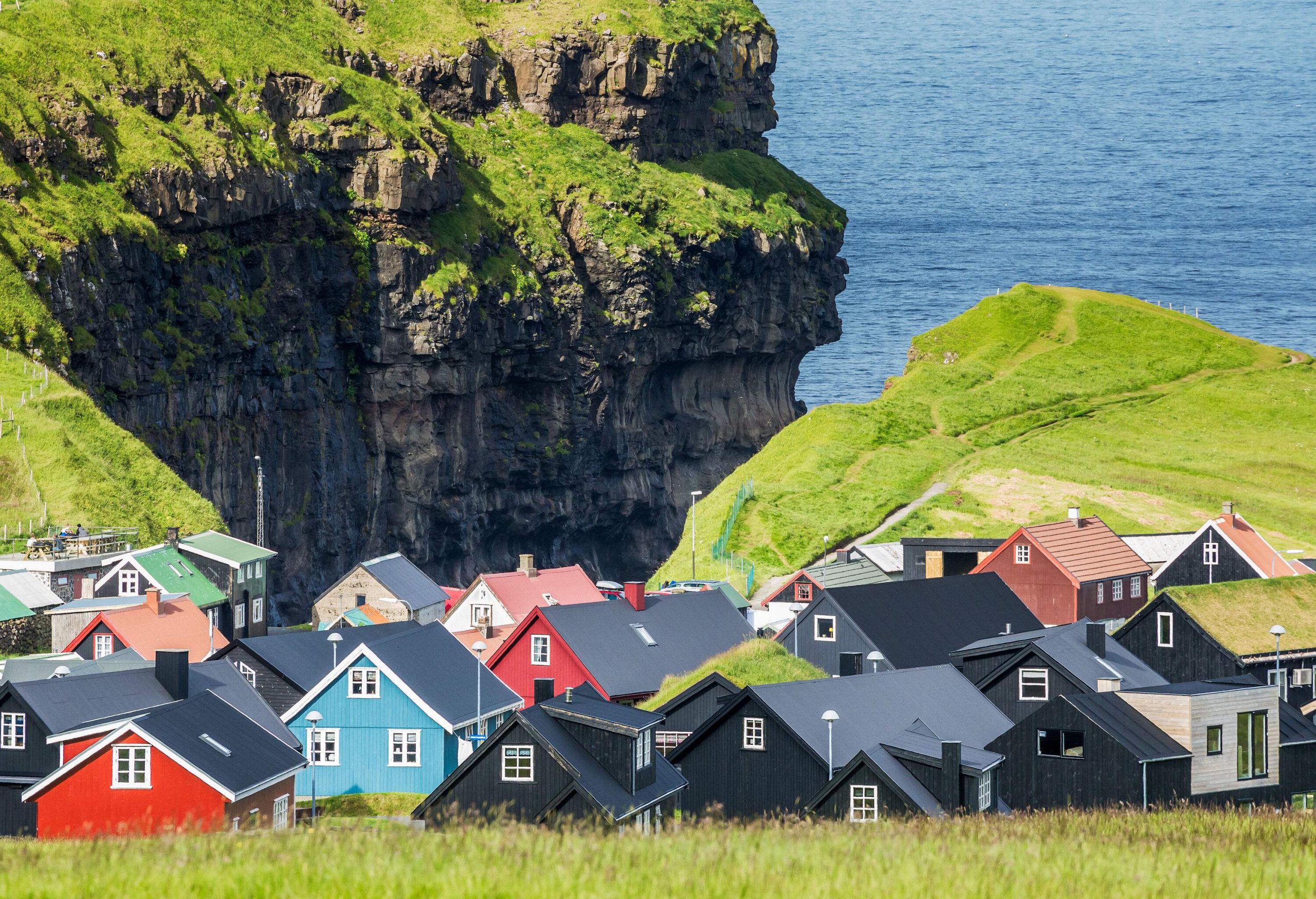 A small village with a cluster of colourful houses lies at the edge of a lush gorge overlooking the sea.