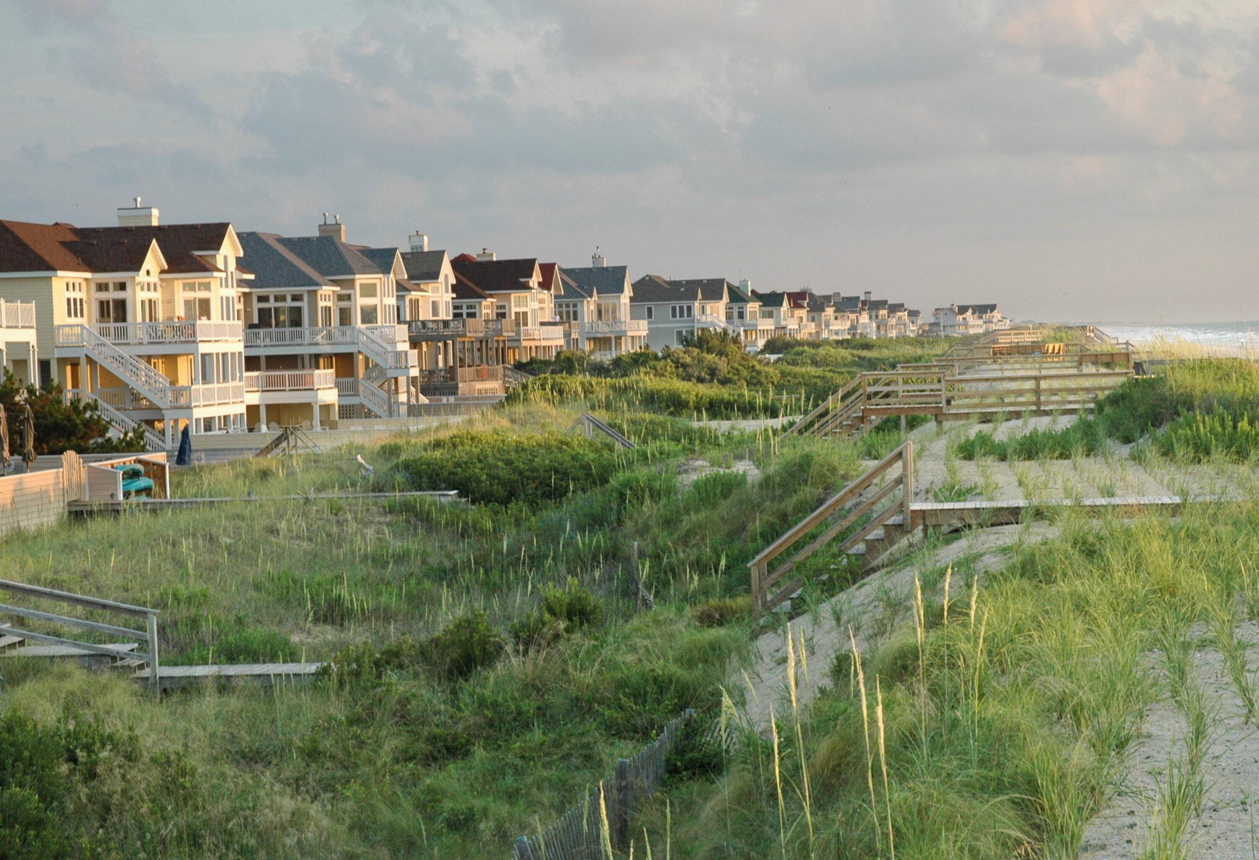 Tall wooden houses line up on the coast with access boardwalks in the bushy dunes to the sea.