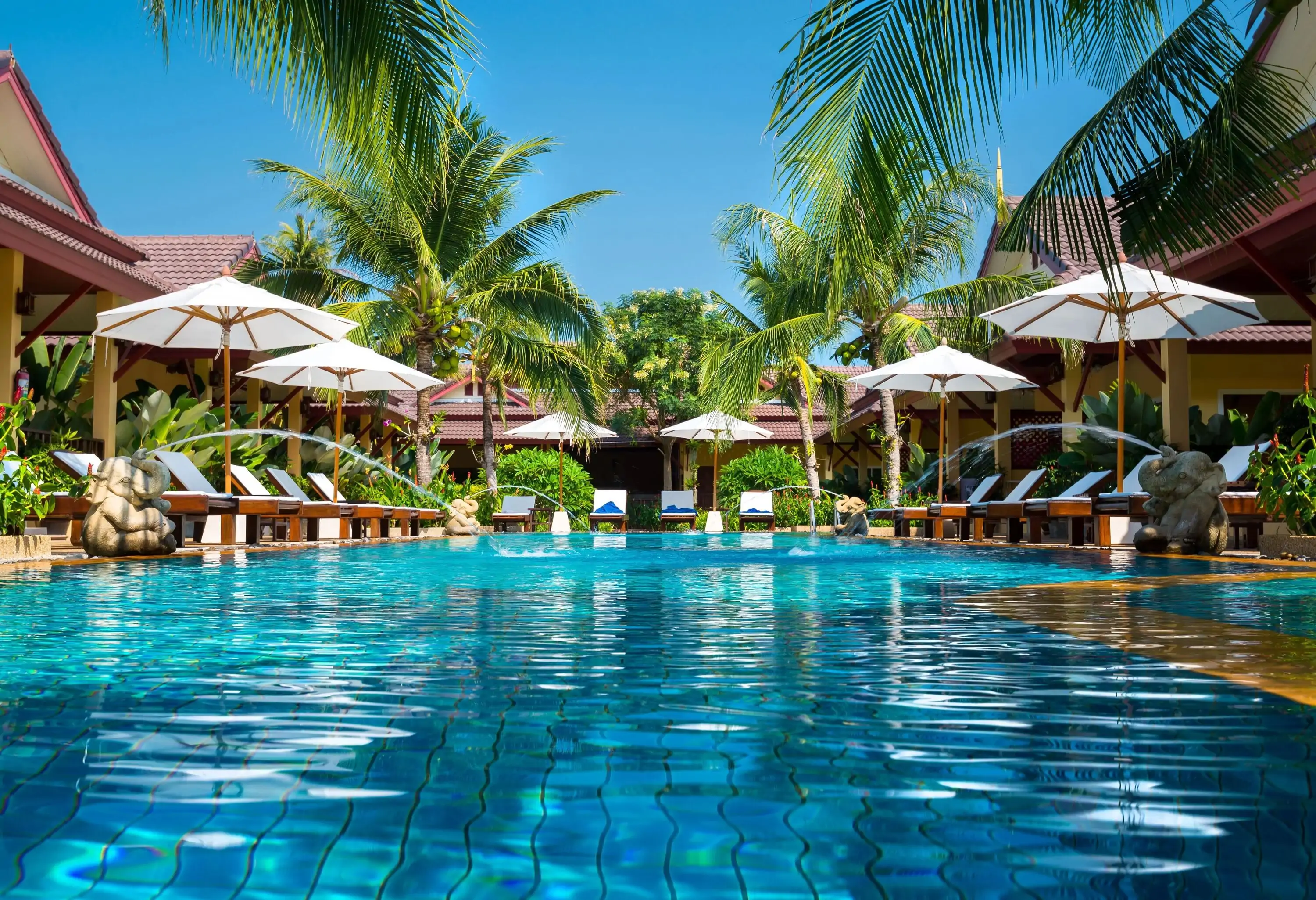 A swimming pool with dazzling clear waters surrounded by sunloungers under white umbrellas.