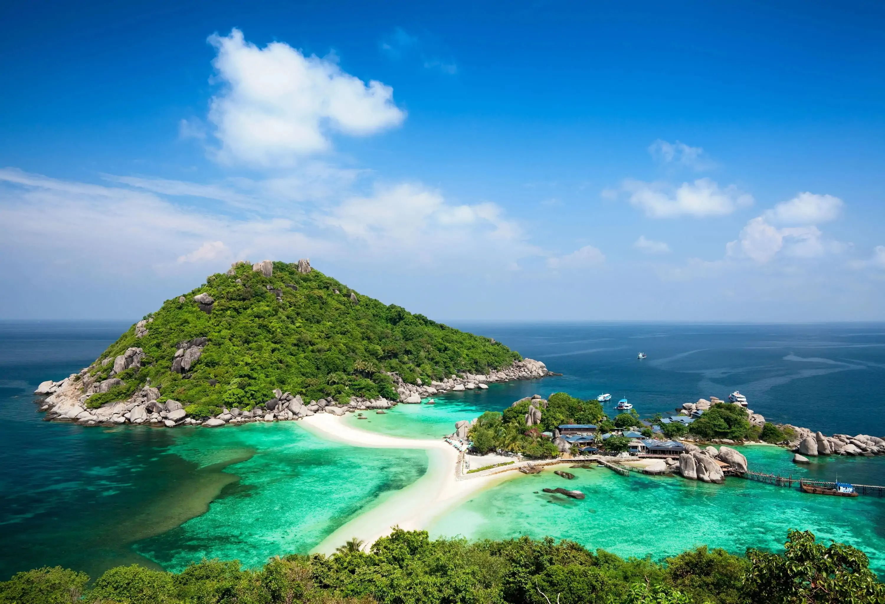 A verdant hill rising majestically amidst the waters next to an island with a striking structure at the pier.