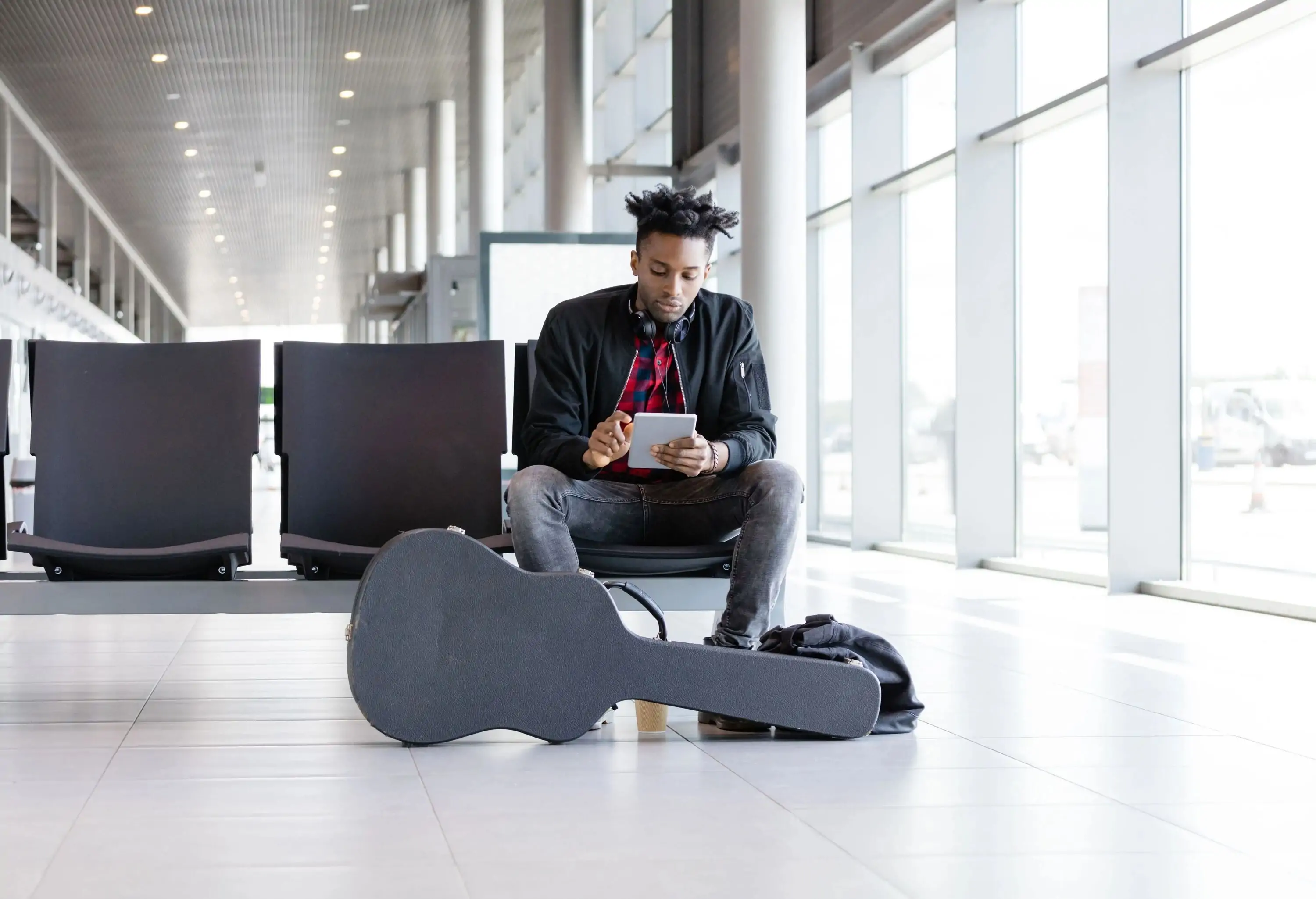 A man traveling with guitar sitting on a chair at the airport