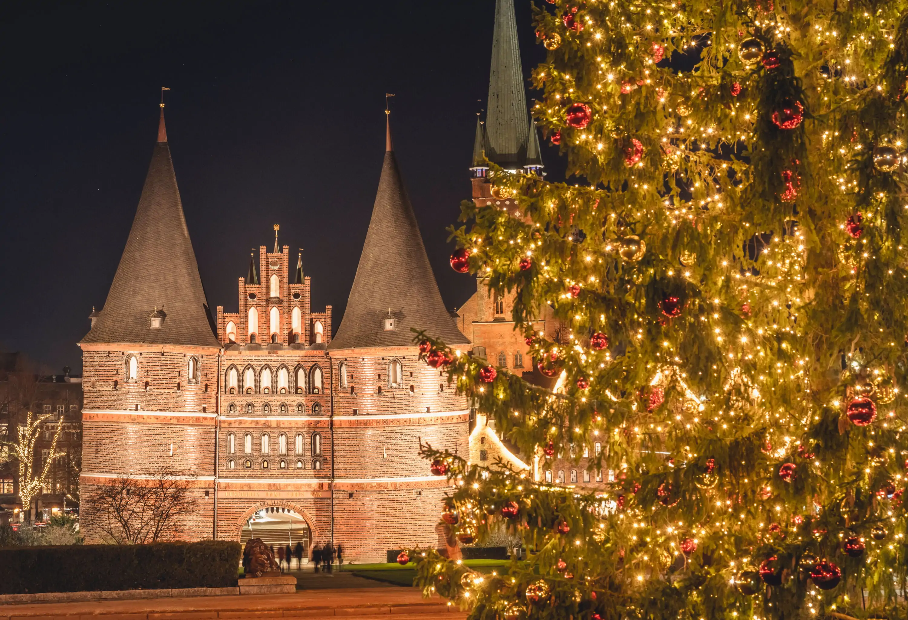 IlluminatedHolstentor gate at night with glowing Christmas tree in foreground