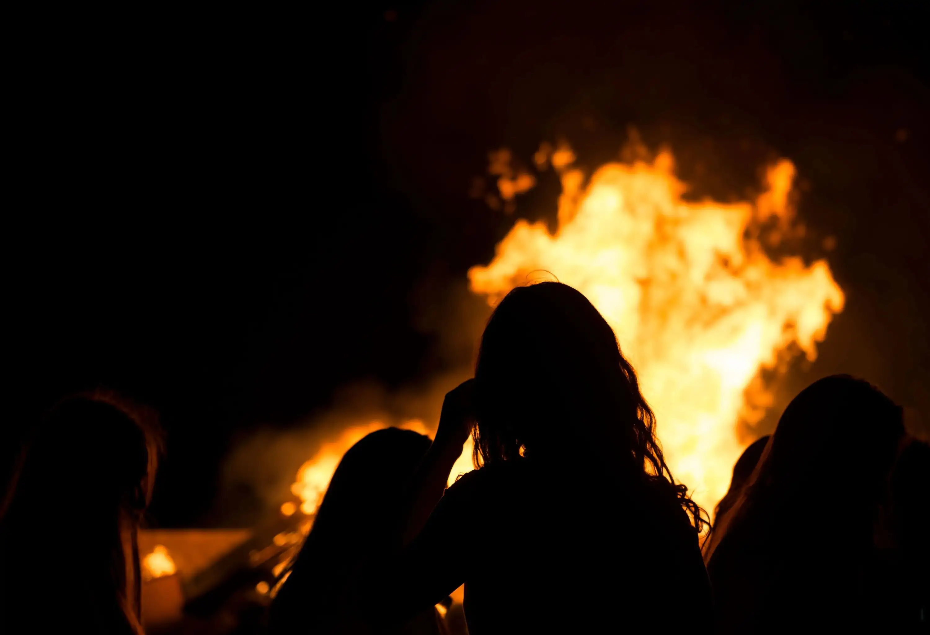 The silhouette of people surrounding the bonfire in the dark night.