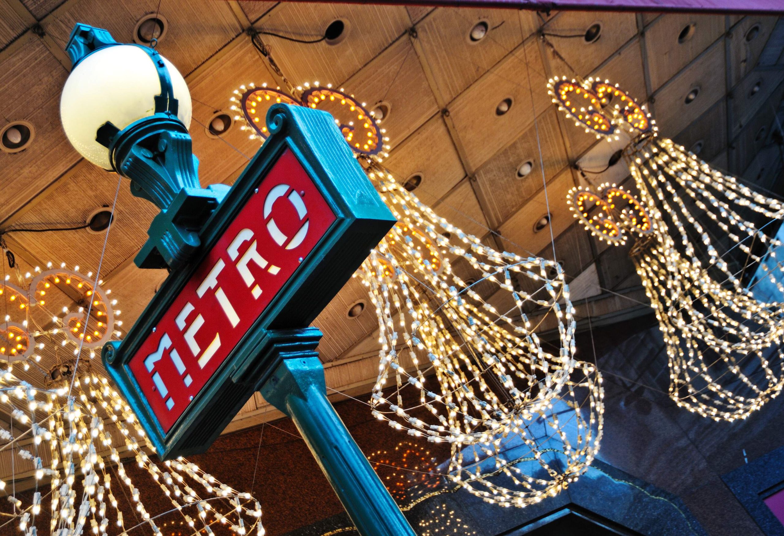 A red metro sign with light ornaments hanging from the ceiling.