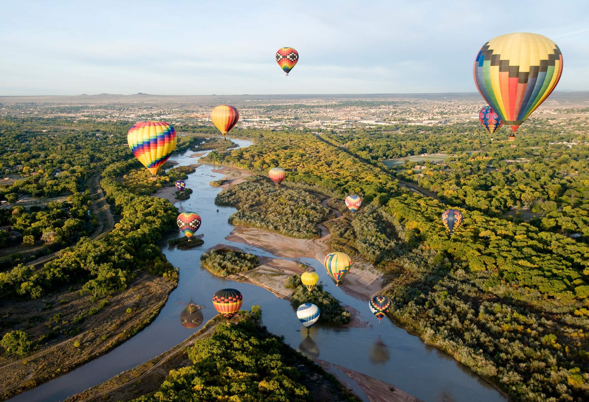Hot air balloons flying over a meandering river surrounded by trees.
