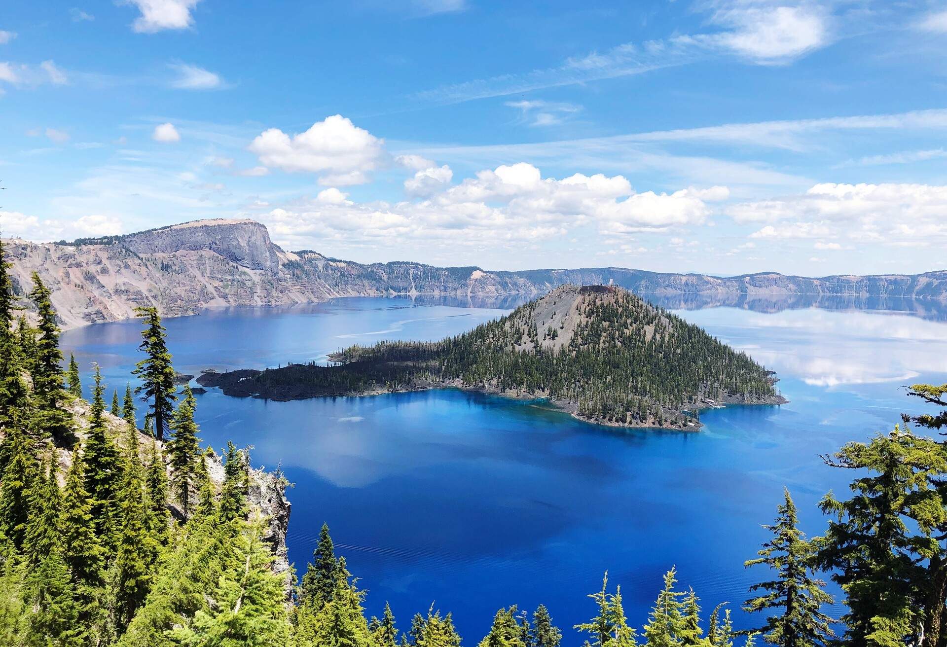 A lake with clear deep-blue water enclosed within mountains and a hill in the middle with green trees.