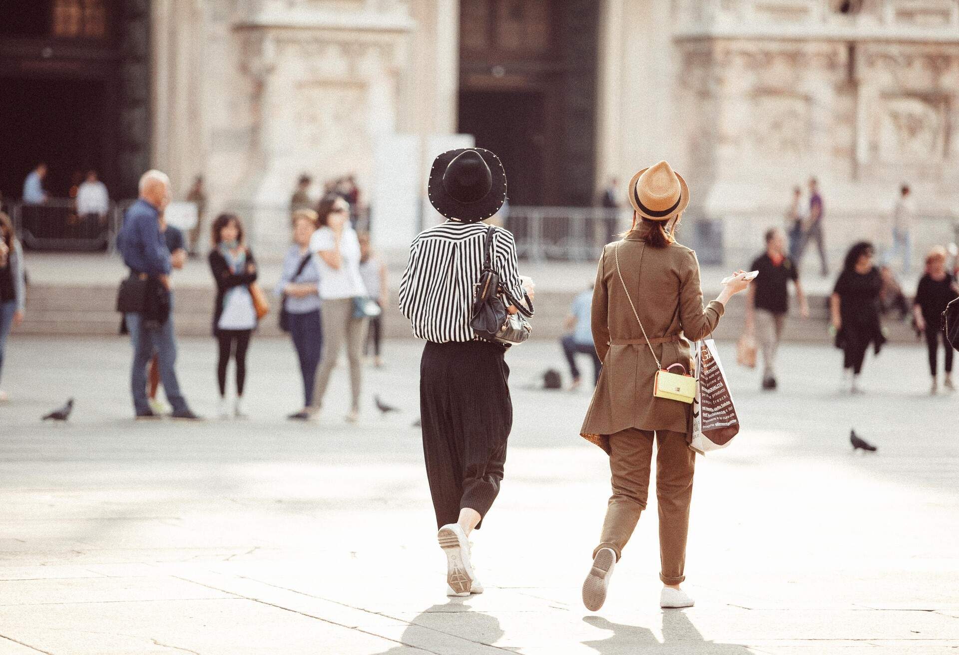 Two stylish women strolling across a town square, admiring the wonderful architecture.