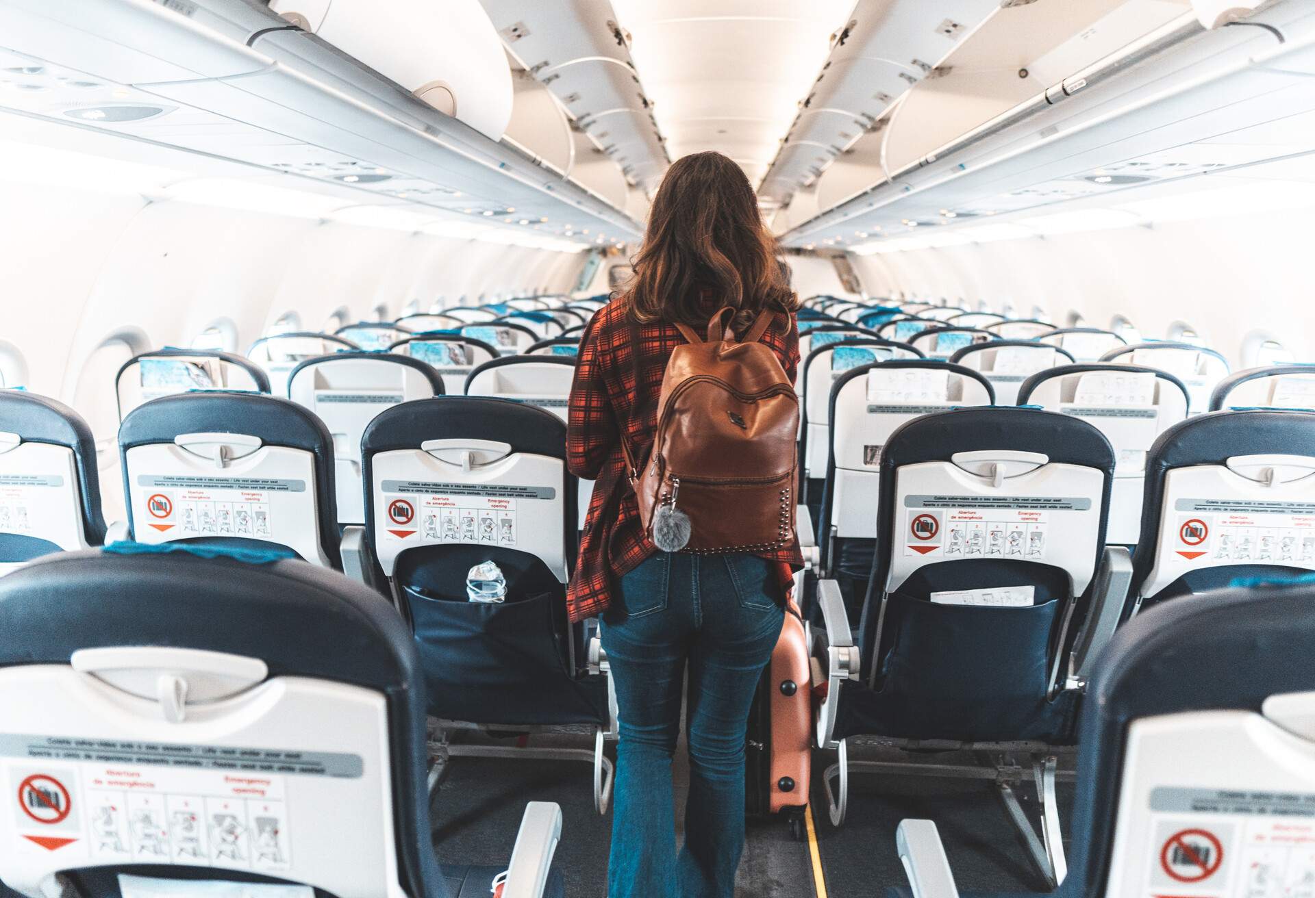 A passenger walks along the aisle of an airplane, passing rows of empty seats.