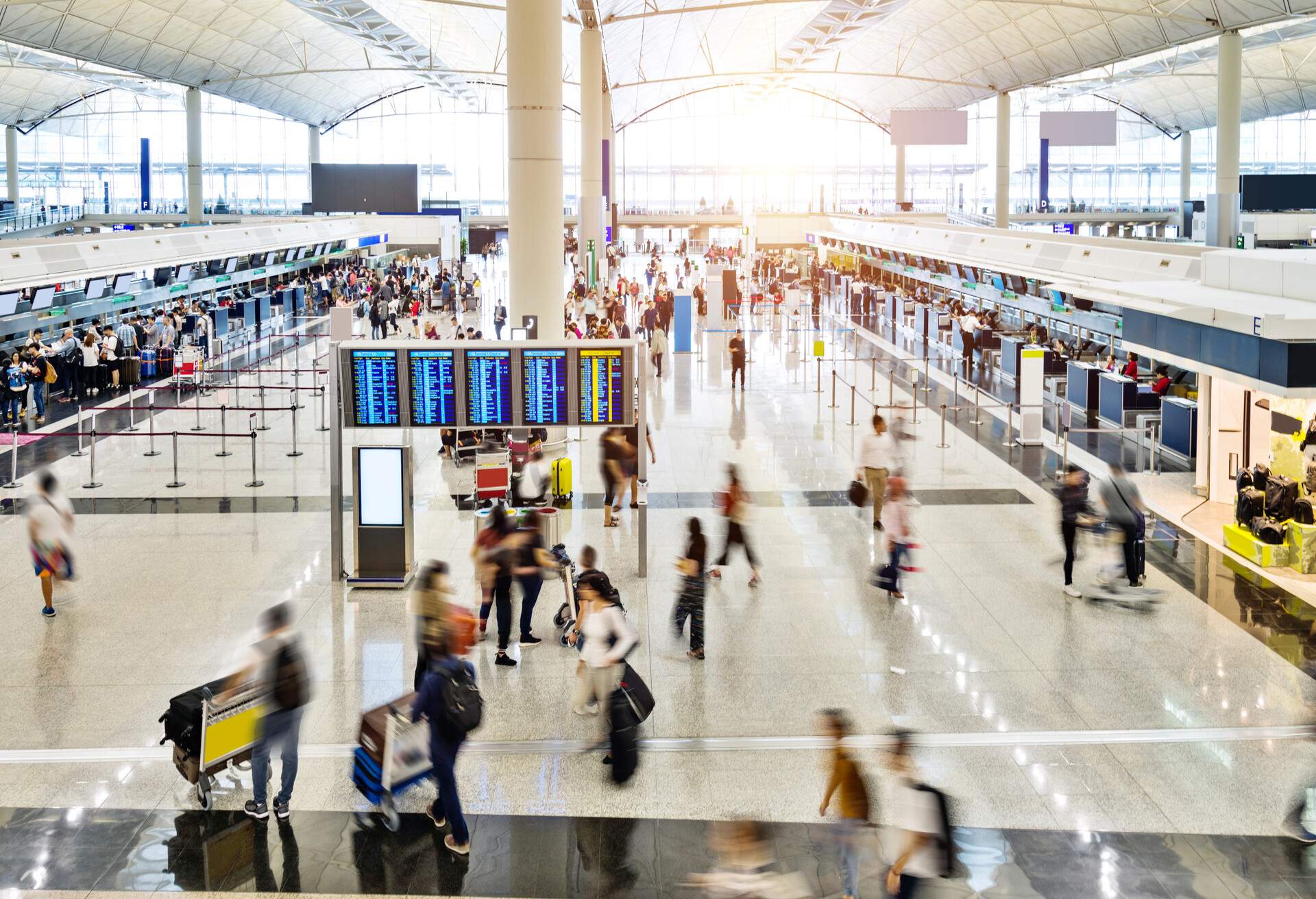 A diverse crowd with their hand carries and luggage, in and out of a busy airport checking area. 