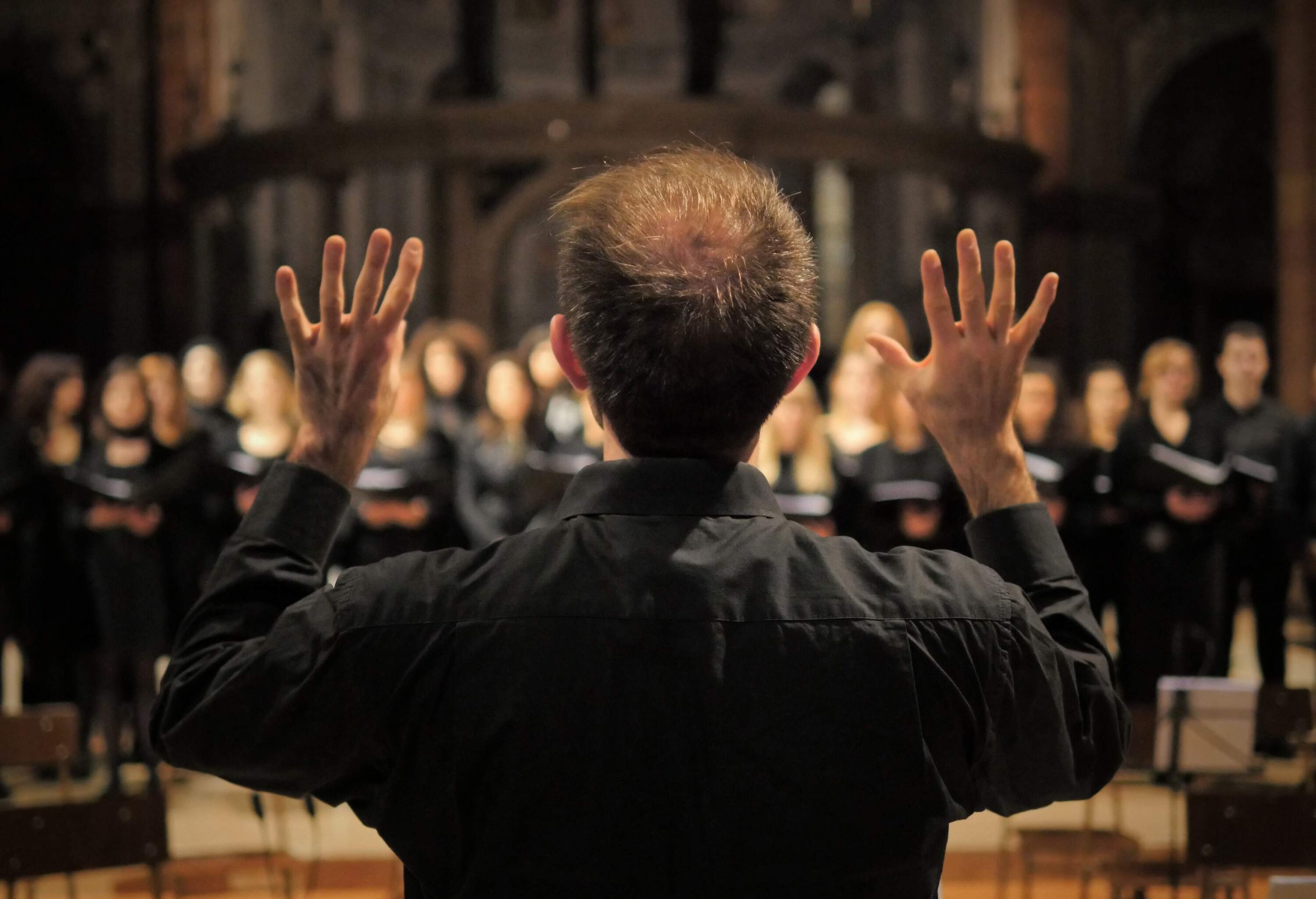 A choirmaster with his hands up against the bokeh of a crowd.