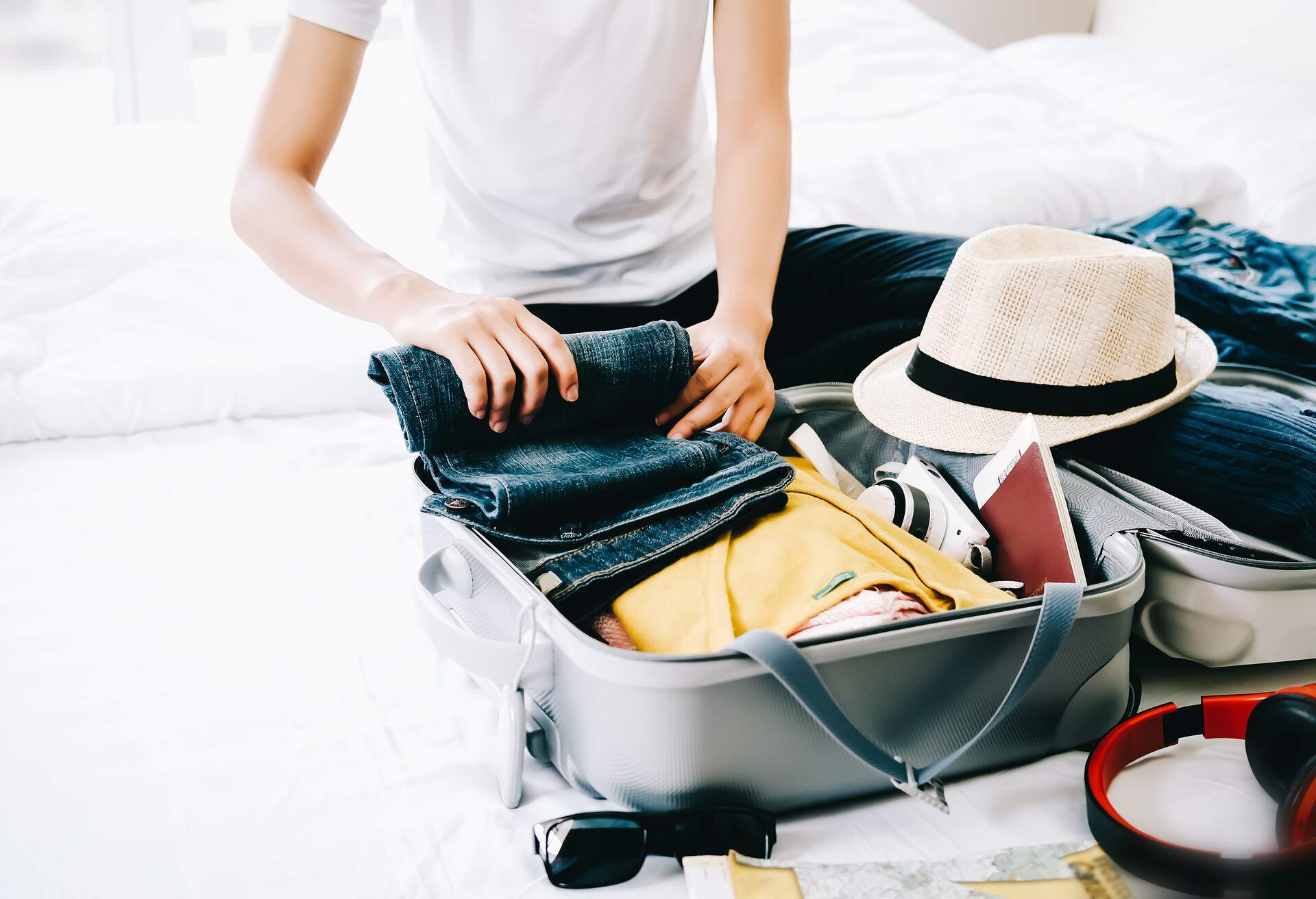 A woman packing her suitcase with clothes, hat, and other travel essentials.