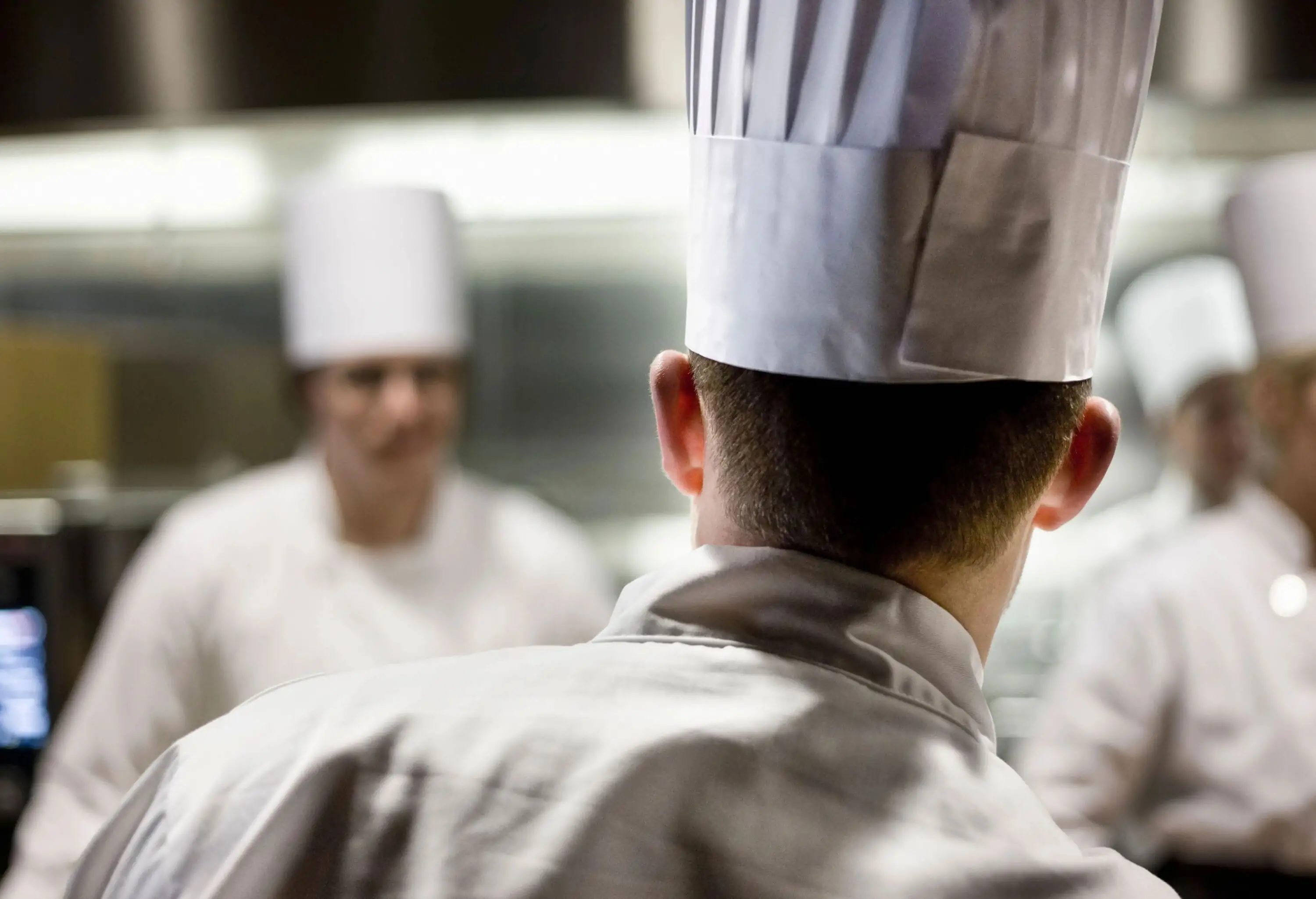 Group of chefs wearing toque hats inside a kitchen.
