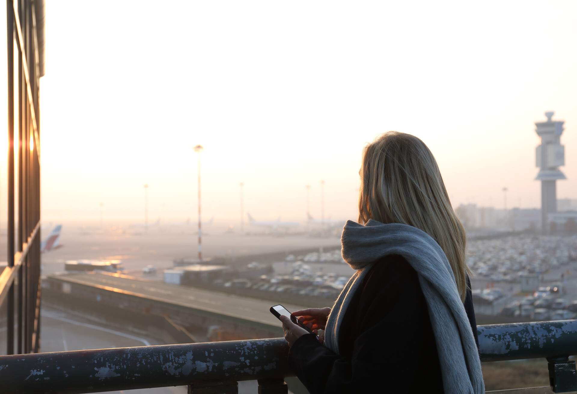 Woman looks out to airport tarmac and sunrise.