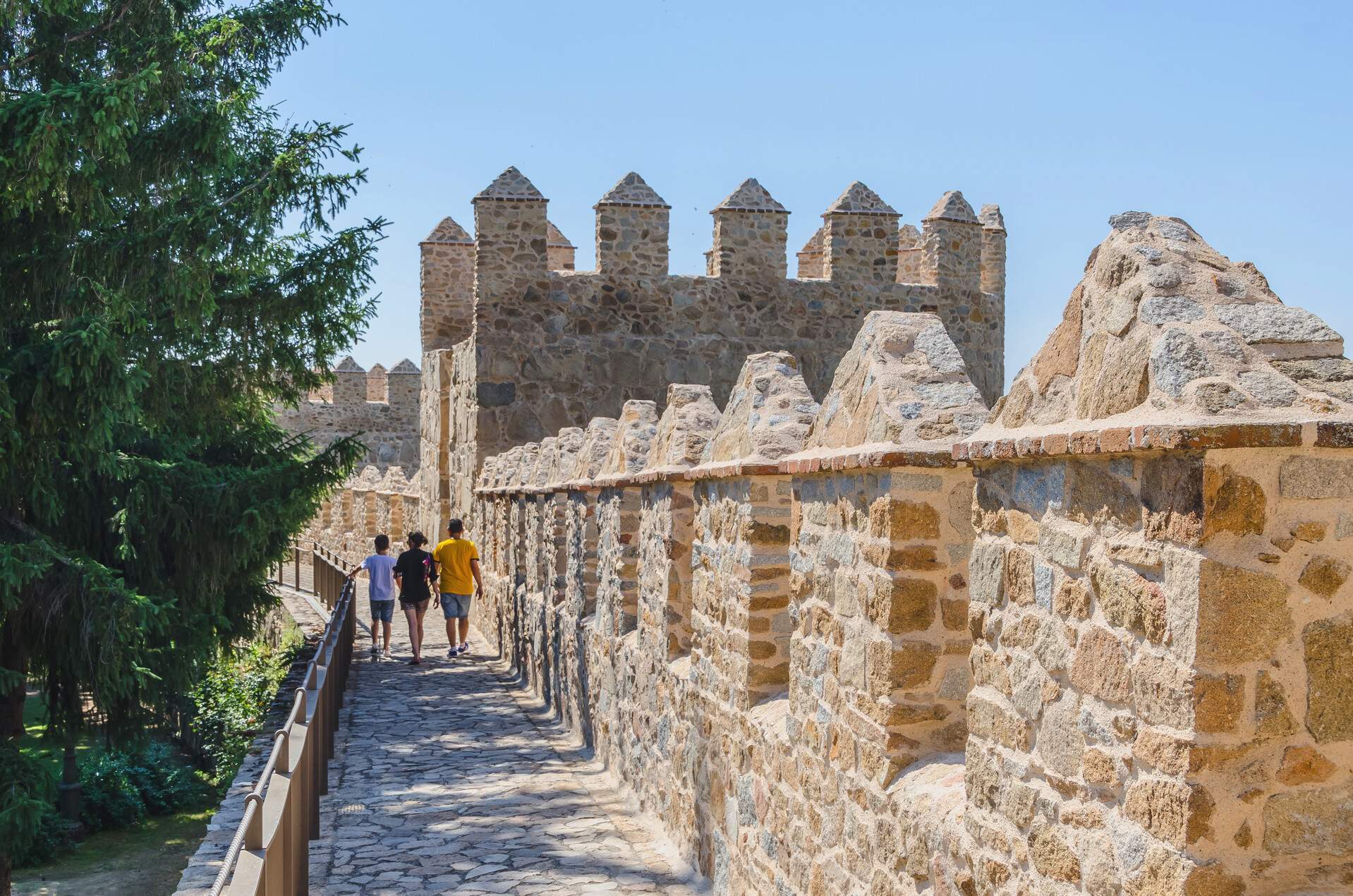 People walk on the footpath by the stone walls of a historical medieval fortification.