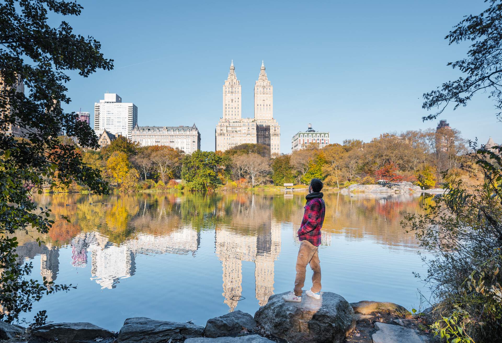 Man standing on rock overlooking lake in central park on a sunny fall day. New York City, USA