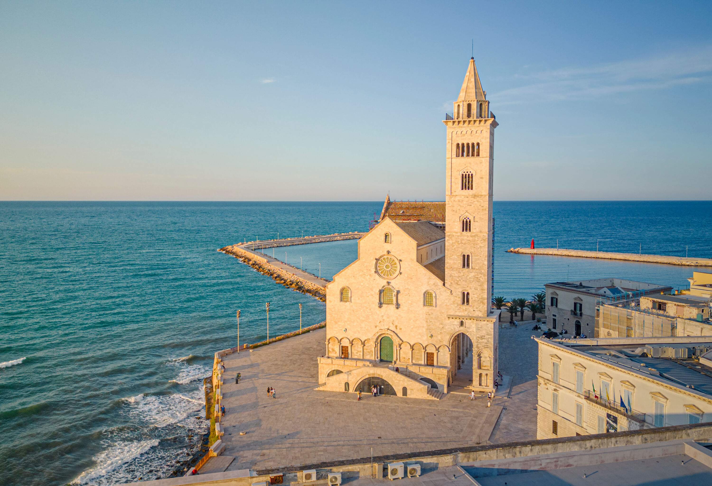 A Romanesque church with a bell tower in a cobbled square along the coast.