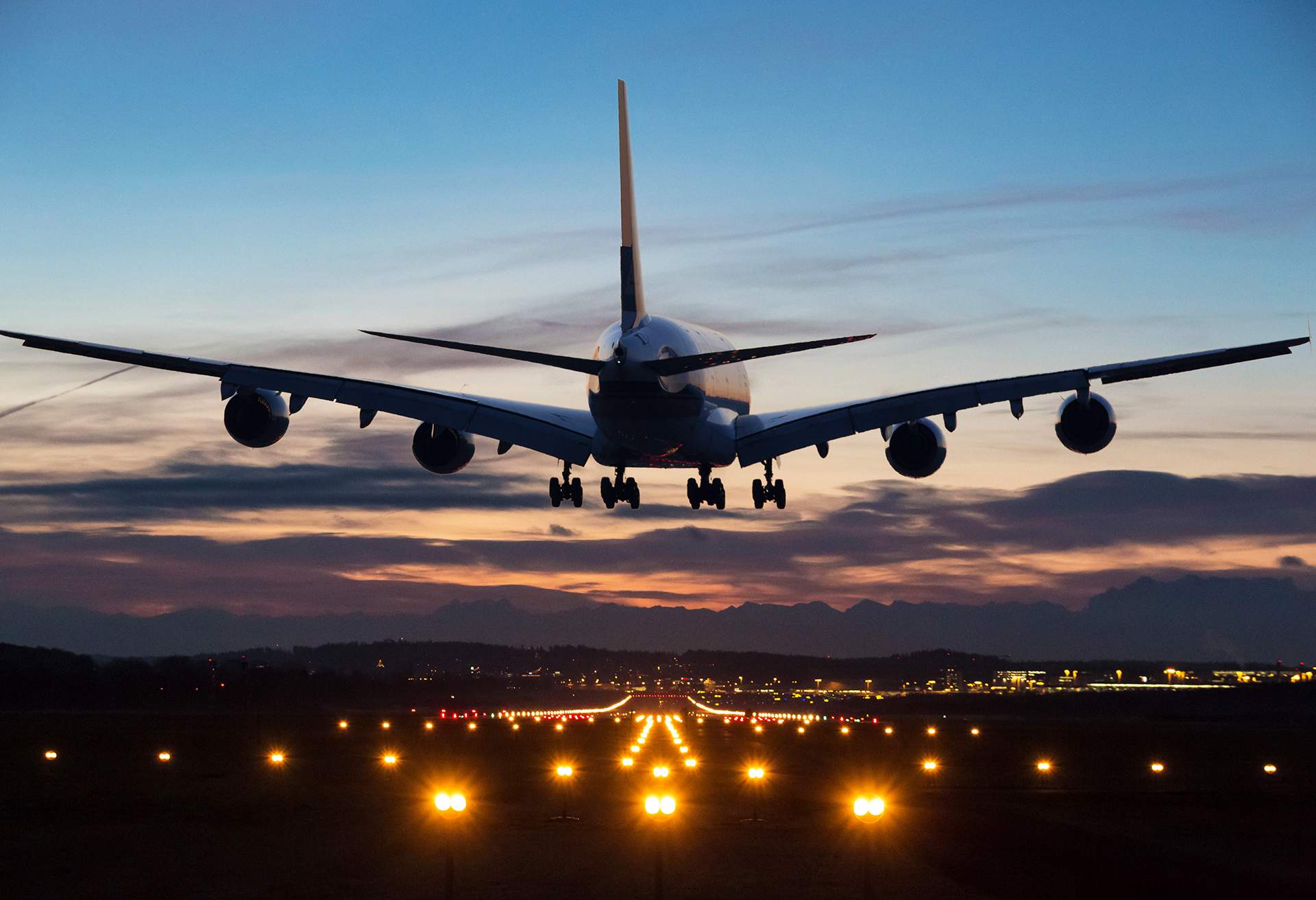 Photo of an airplane just before landing in the early morning. Runway lights can be seen in the foreground.