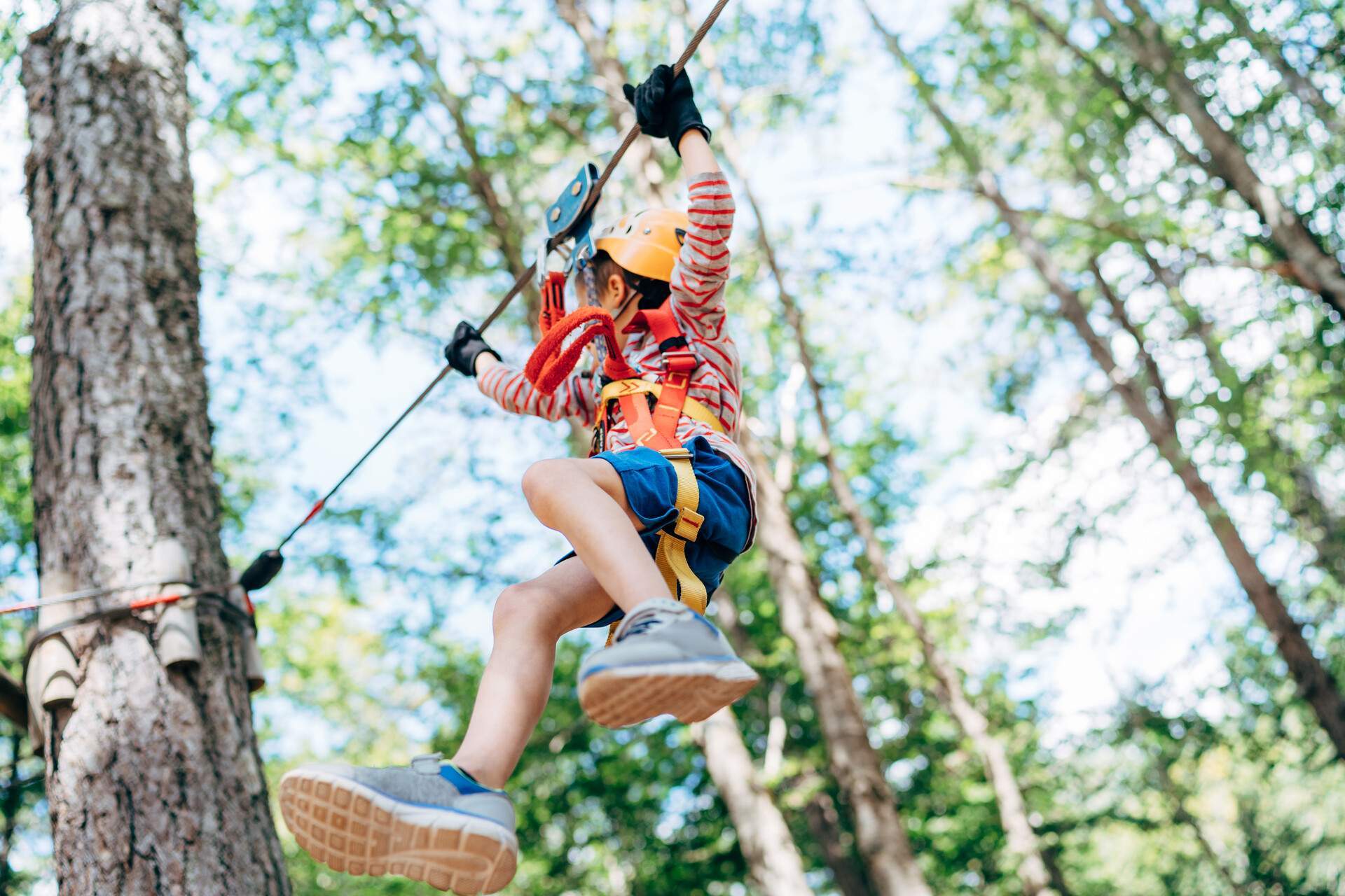 A kid hanging on the zipline holds on to the rope tight approaching a tree.