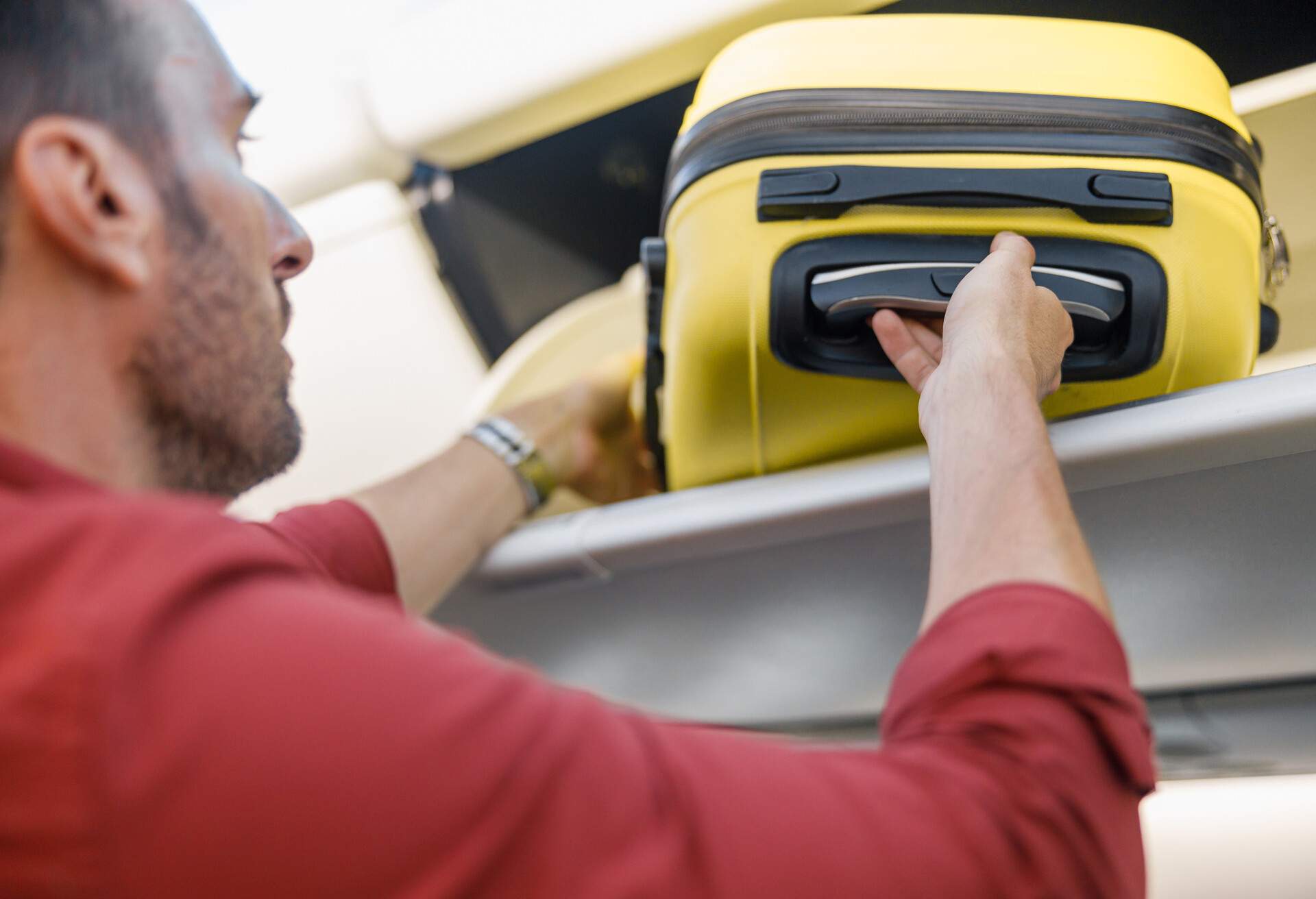 Man pulling out hand luggage from compartment while traveling by plane.