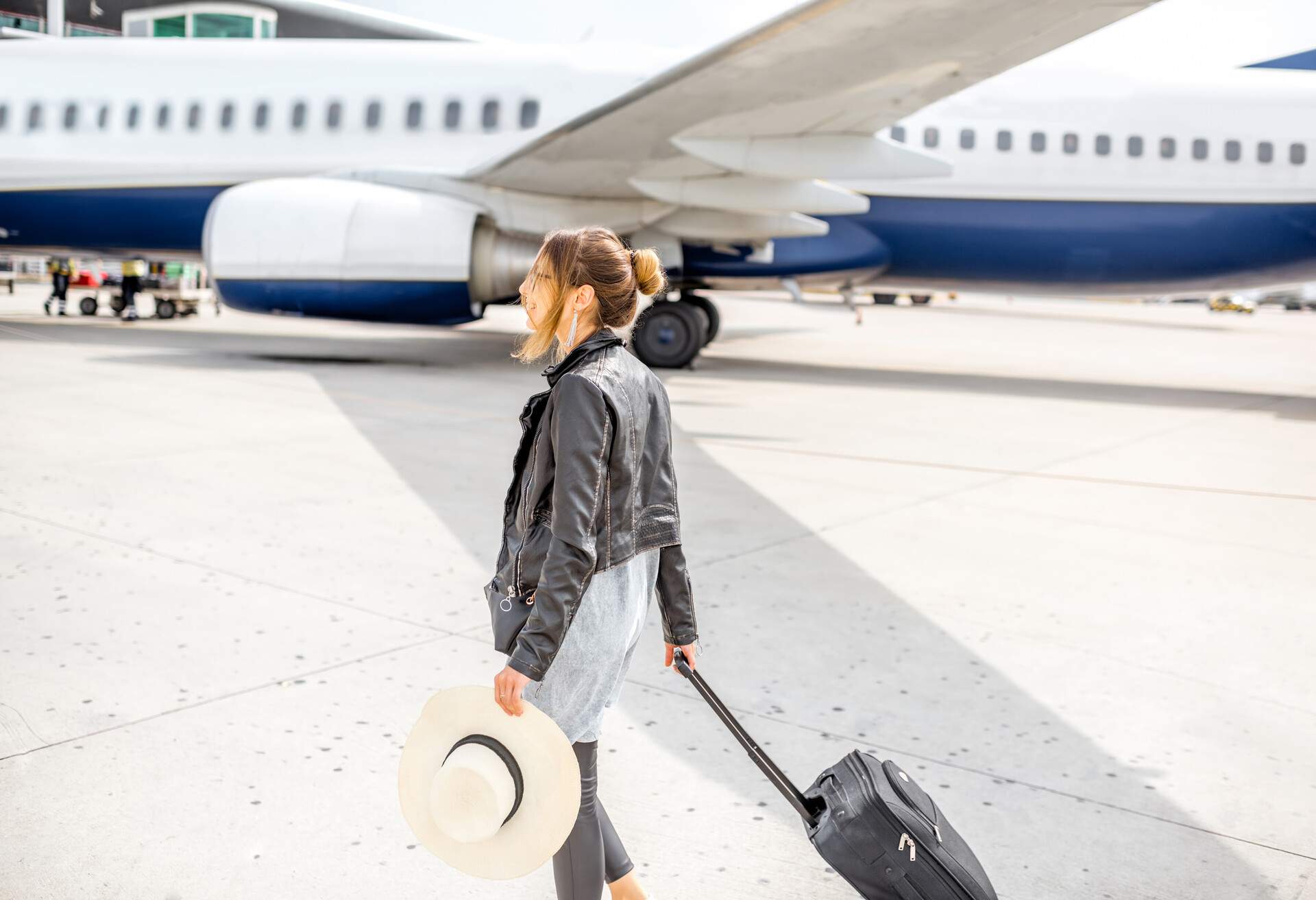 Woman boarding flight with carry on luggage and hat