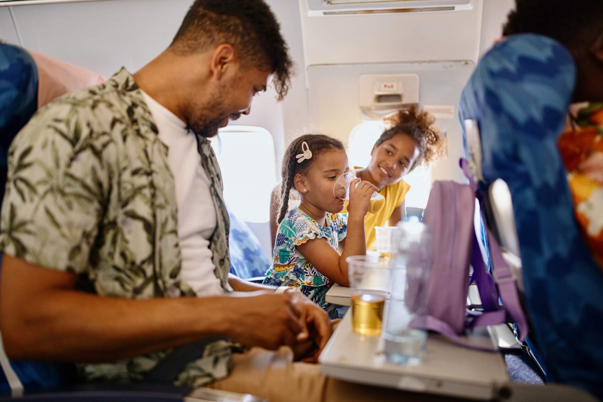 A man and two young girls having drinks on a plane.