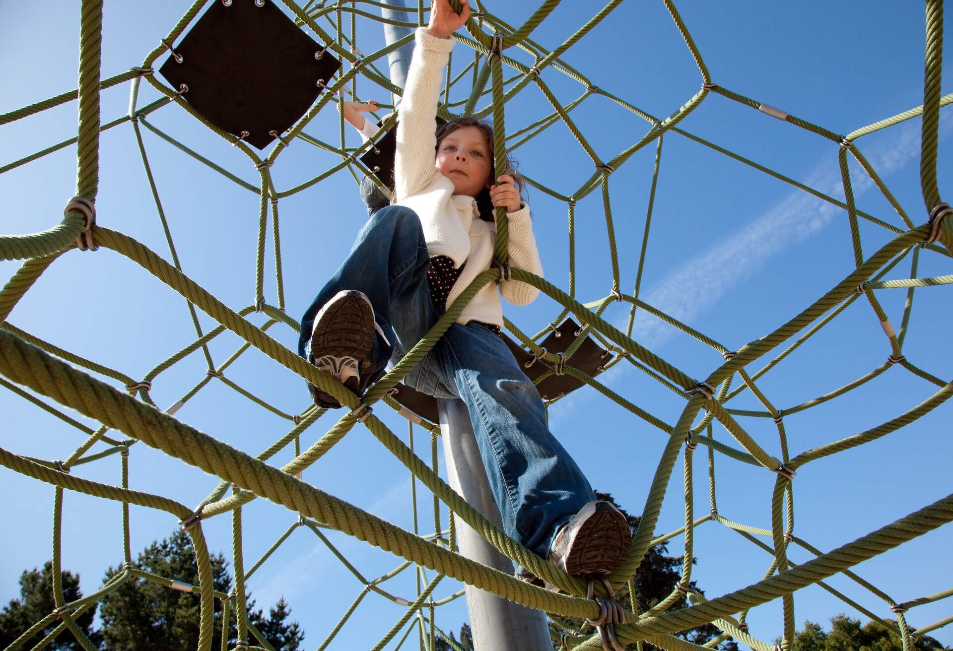 A girl climbing on a playground set with blue sky in the background.