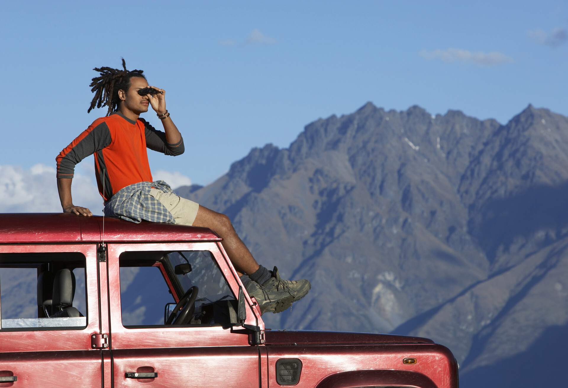 Man standing on 4x4 rental car looking through binoculars in New Zealand's South Island