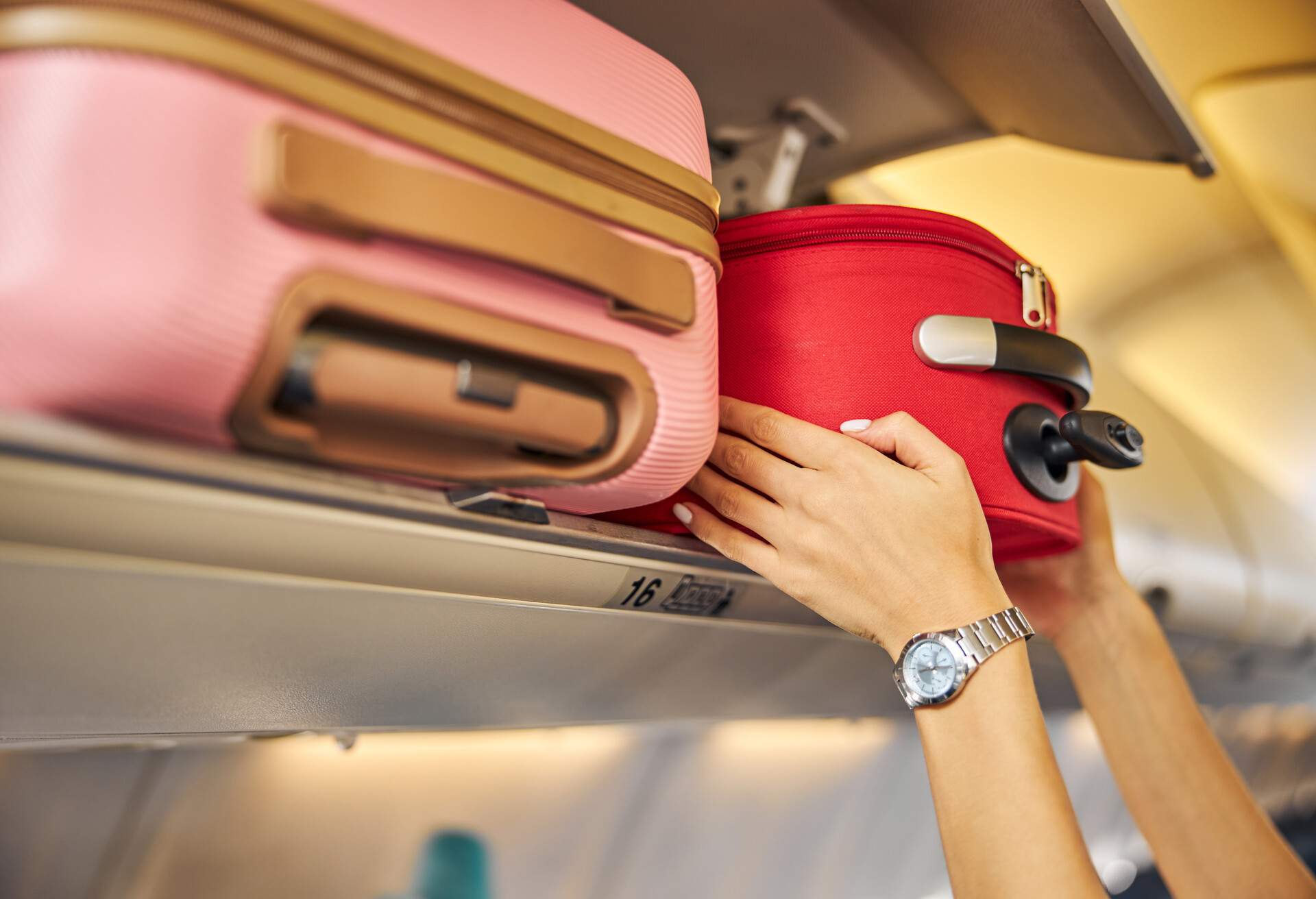 Arms shoving a small piece of luggage to the top shelf of an aircraft.