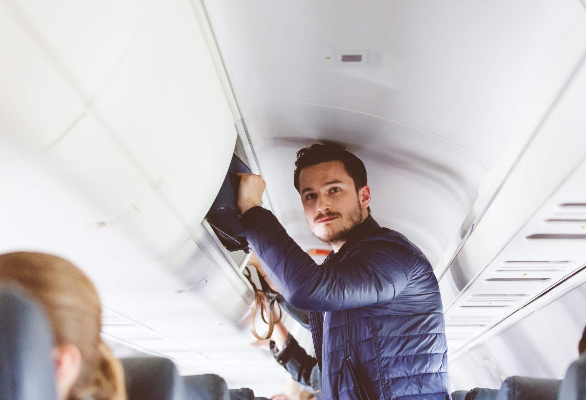 Plane passenger storing hand luggage in the overhead locker. People travelling by flight.