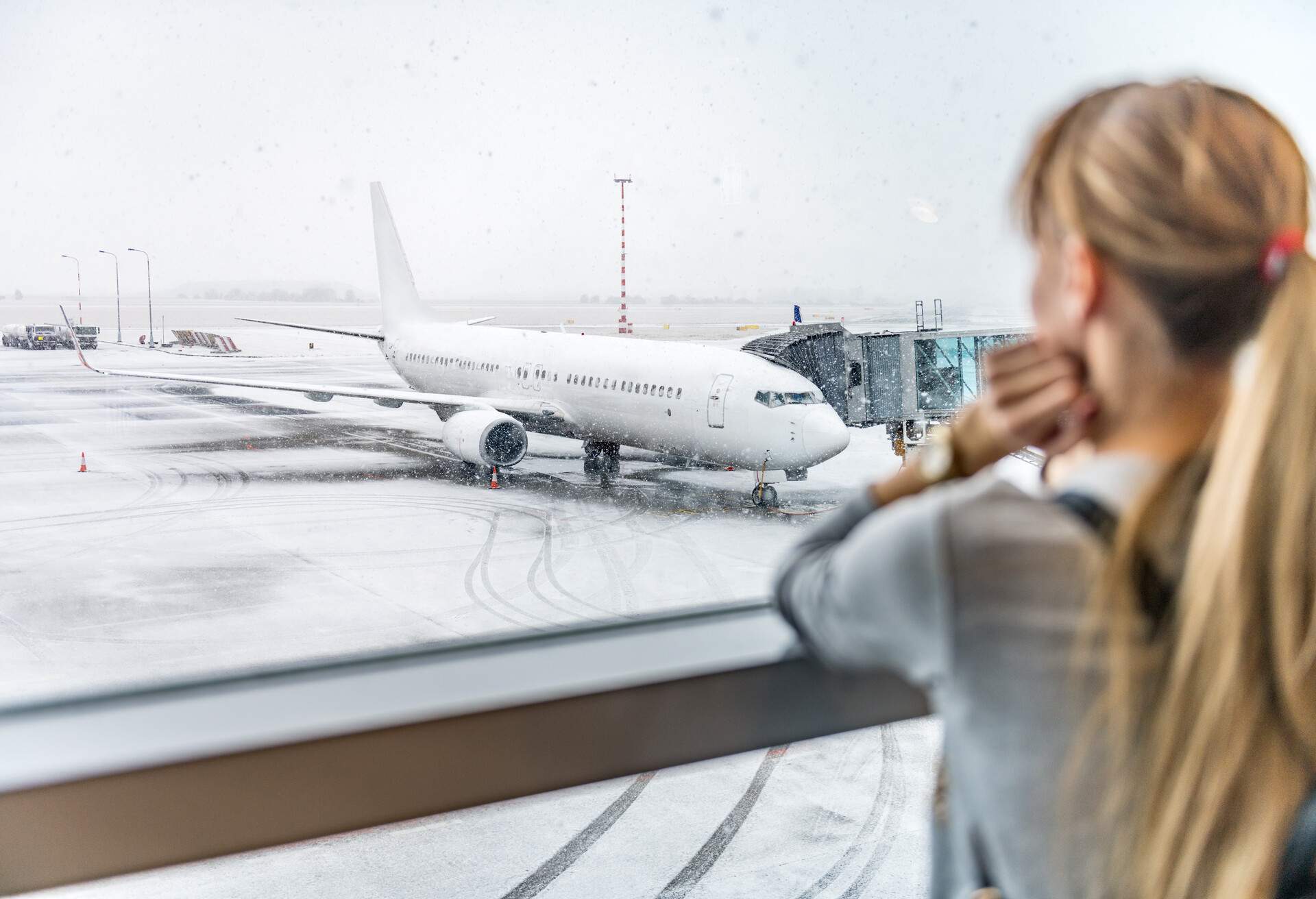 Horizontal color image of airplane during snowstorm and woman looking and waiting for departure.