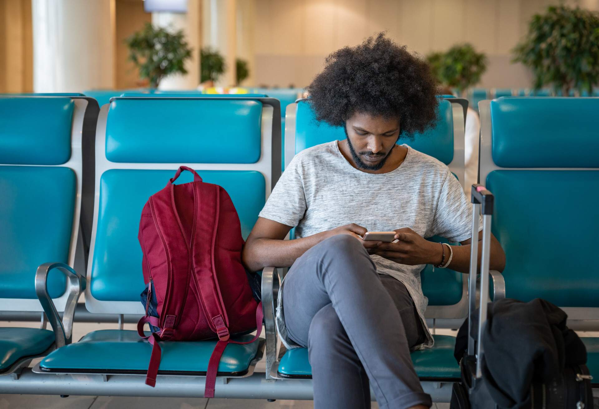Portrait of a male traveler at the airport using his cell phone while waiting for his flight and smiling.