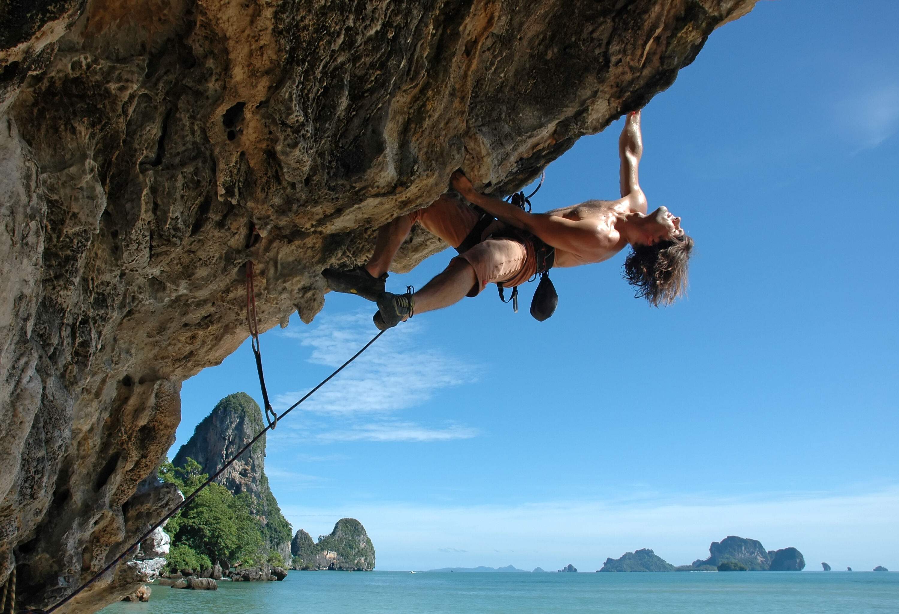 A rock climber clings on an overhanging rock wall with safety ropes.