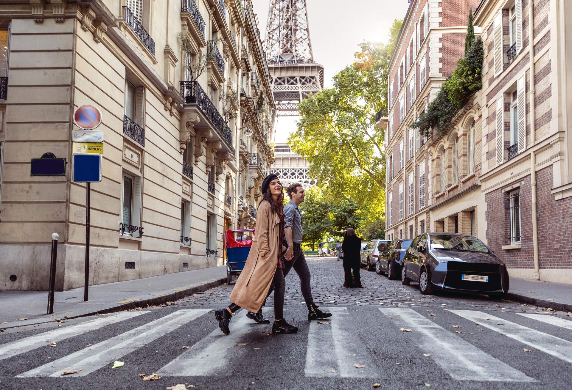 A couple dressed casually crosses a pedestrian crosswalk with the Eiffel Tower in the background.