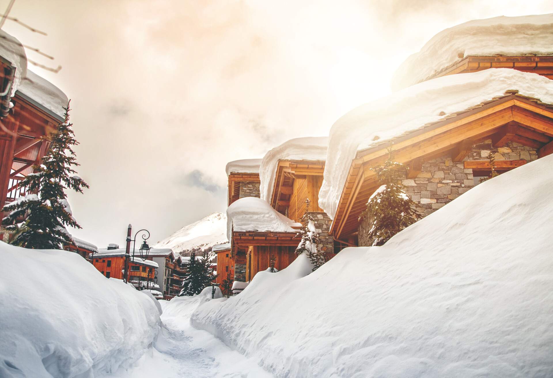 Several houses with stone walls and wooden roofs, connected by a snowy path.