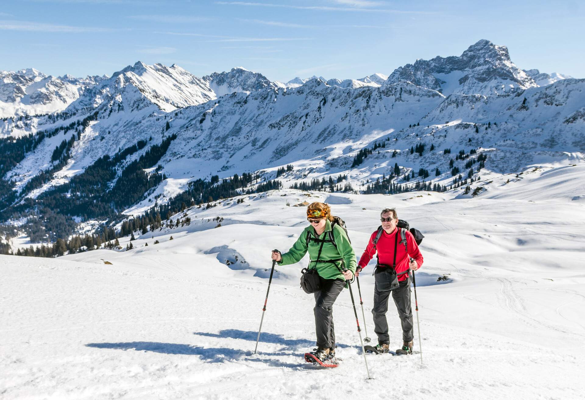 A couple of hikers traversing a snowy landscape with icy mountains in the background.