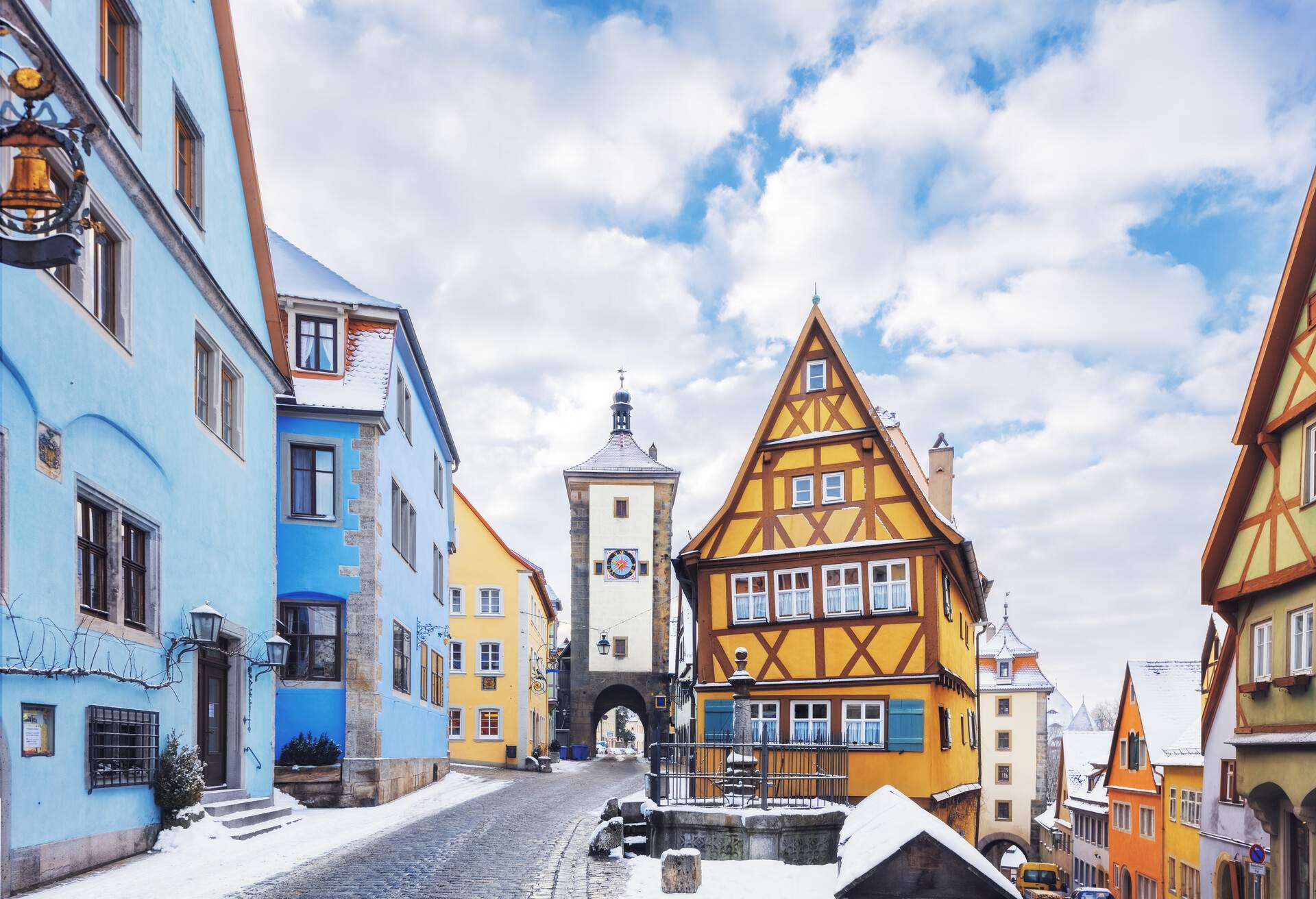 Colourful half-timbered houses lining a cobblestone street with a snow-covered sidewalk. 