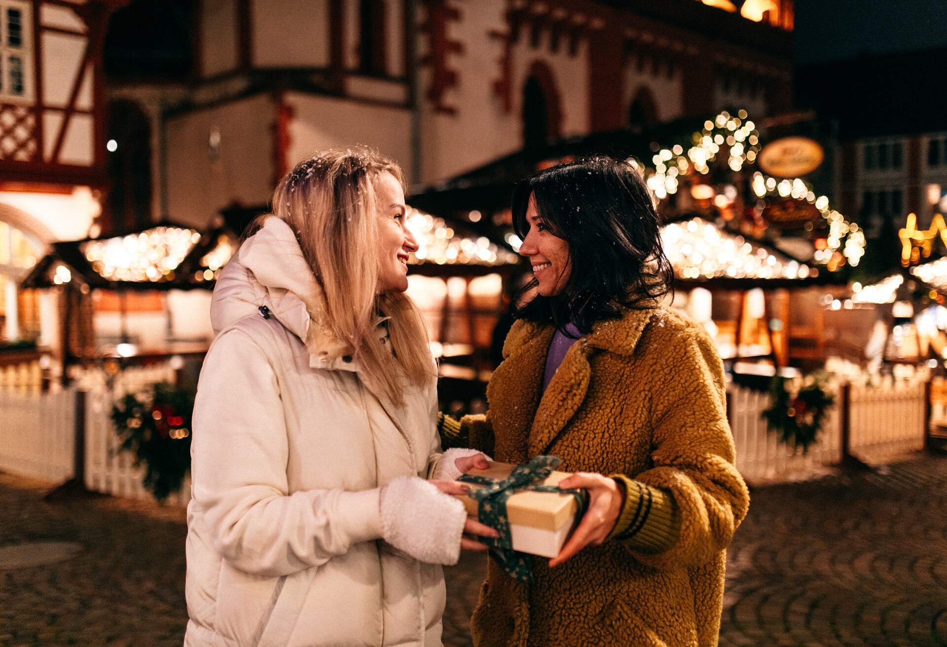 Two women in winter jackets smile while holding a wrapped gift.