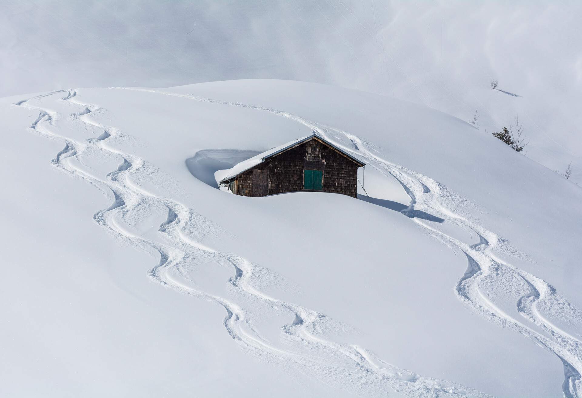 A hillside cabin buried in deep snow with ski tracks.