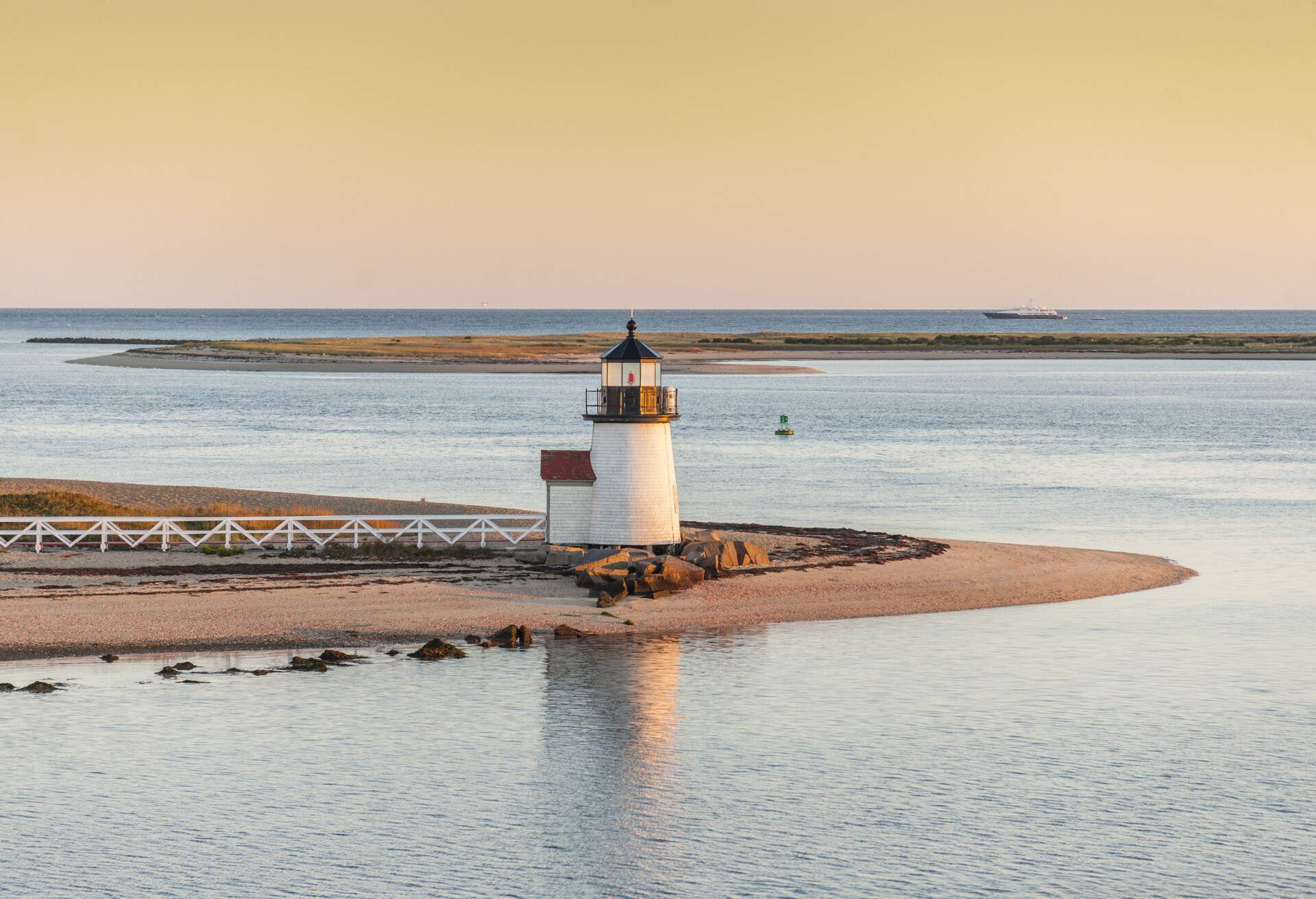A stout lighthouse at the tip of an island surrounded by tranquil waters.